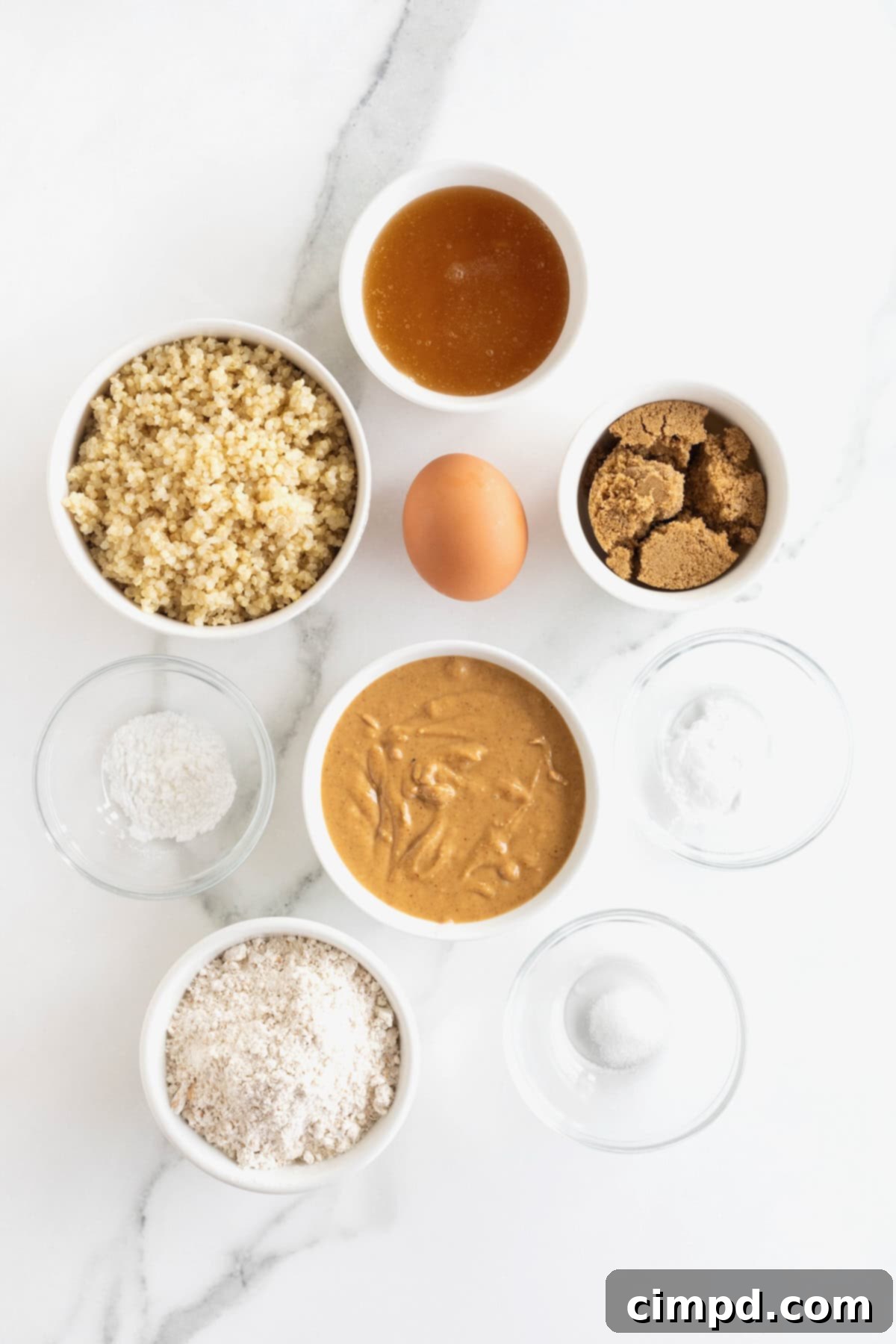 Wholesome Peanut Butter Quinoa Cookies 5 A collection of small white and glass dishes holding the fresh ingredients to make peanut butter quinoa cookies, neatly arranged on a pristine white marble counter, ready for baking.