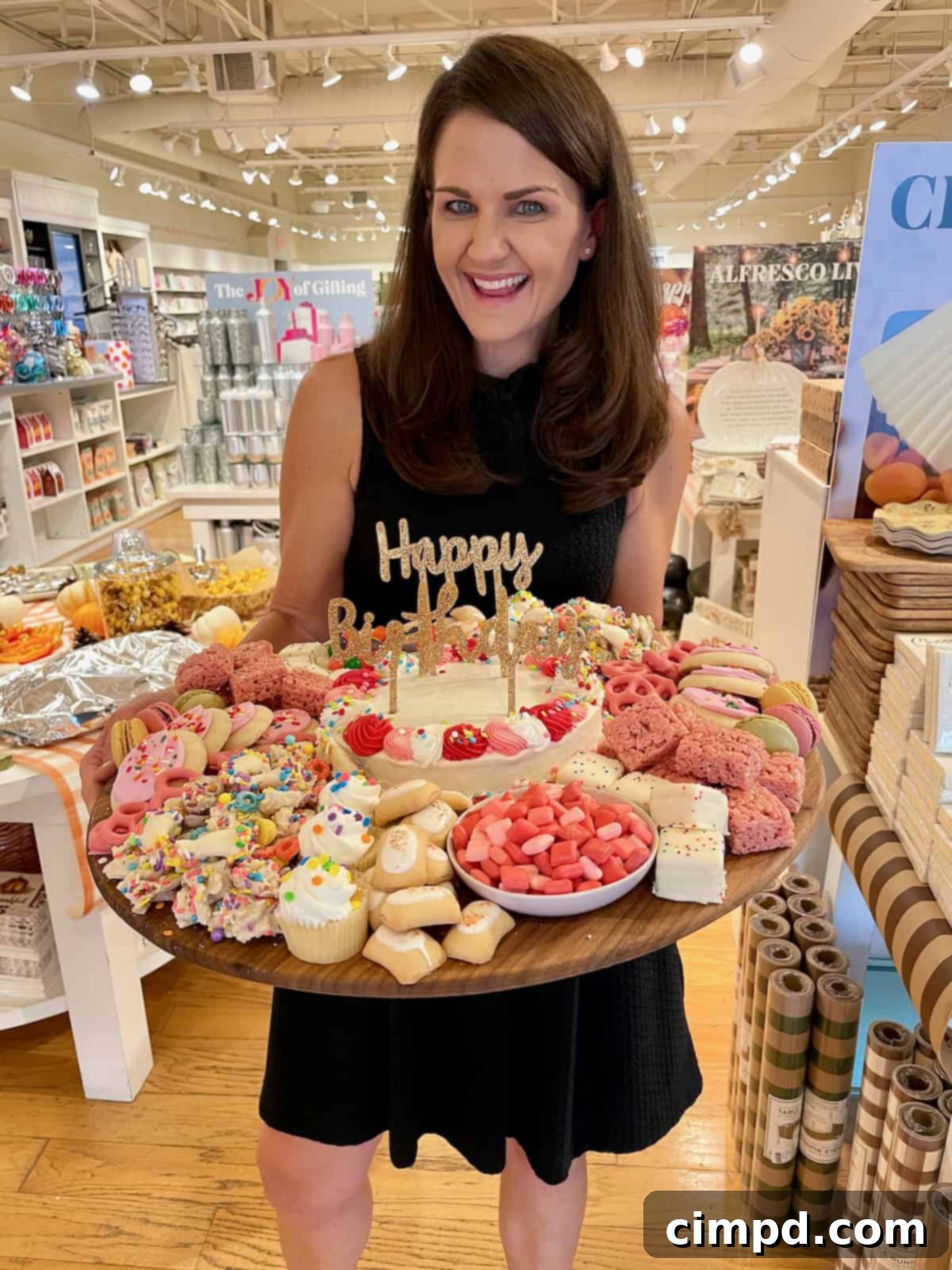 Maegan Brown proudly holding a festive birthday dessert board overflowing with colorful treats, celebrating the success of her cookbook.