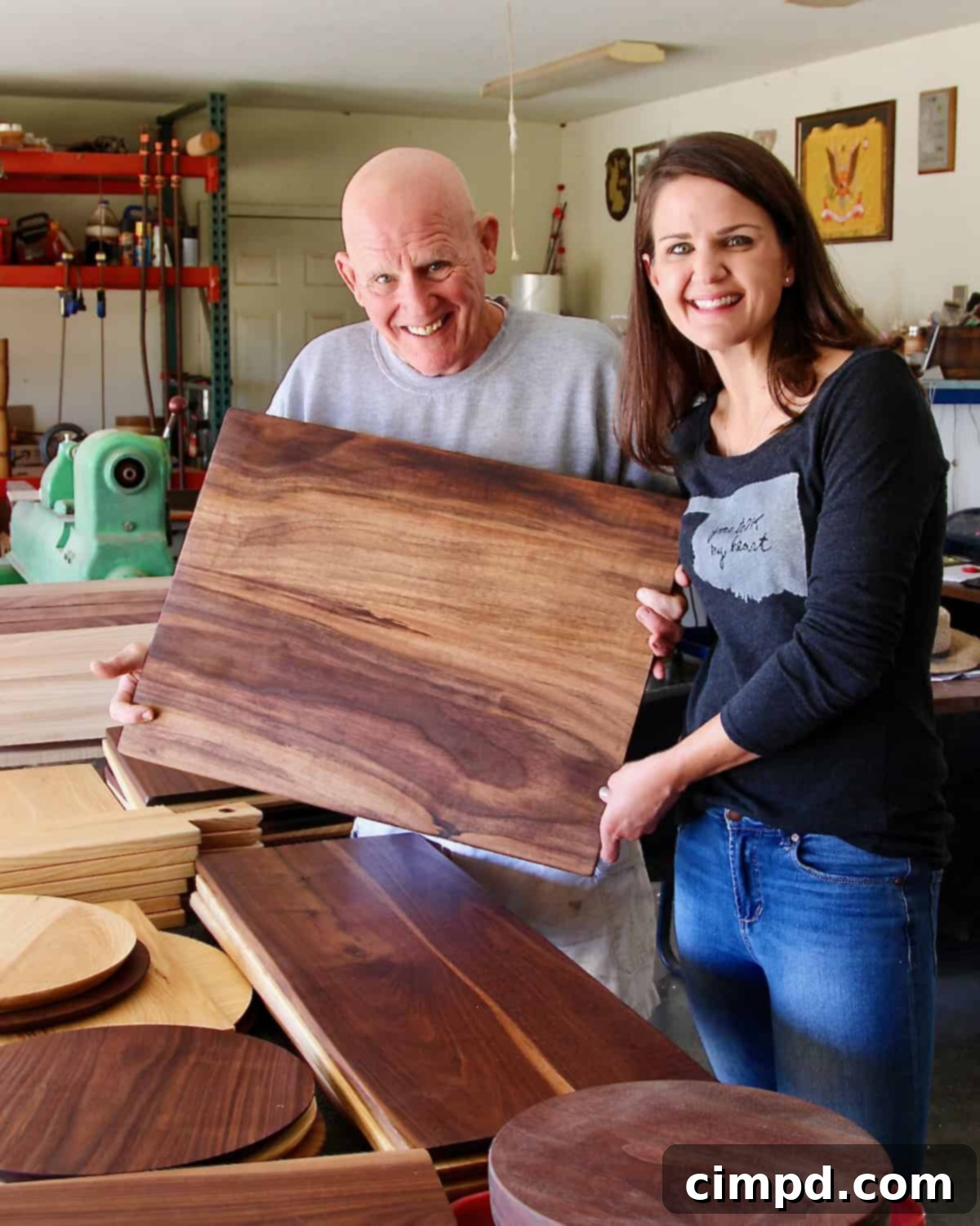Maegan Brown and her father proudly pose with a meticulously crafted wood board in his workshop, showcasing their collaboration.