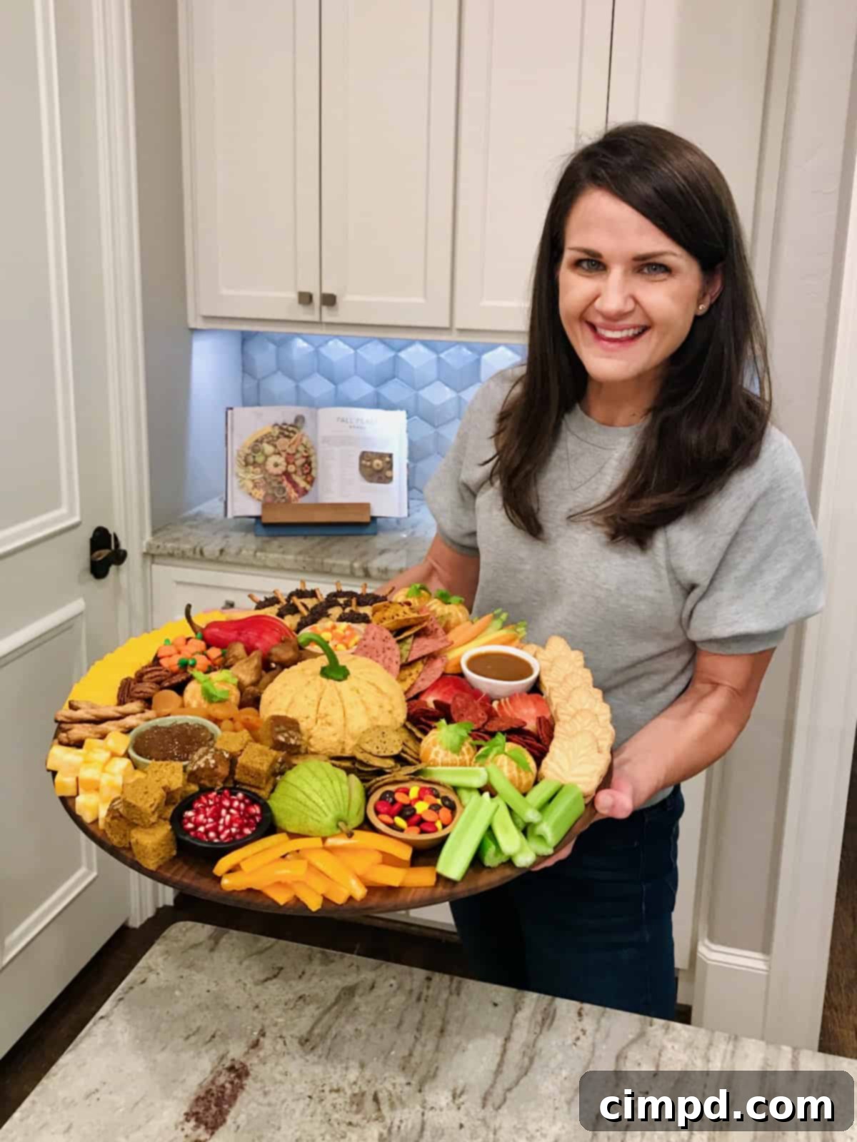 Maegan Brown holding a festive Fall themed snack board, adorned with autumnal treats and seasonal decor, perfect for cozy gatherings.