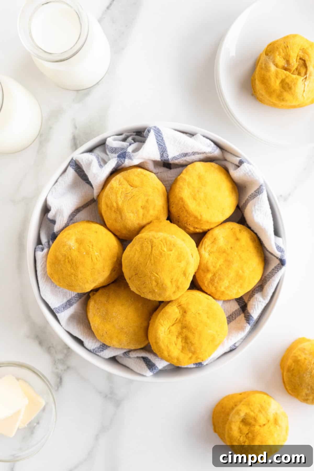 A large white serving bowl lined with a tea towel filled with golden-brown pumpkin biscuits.