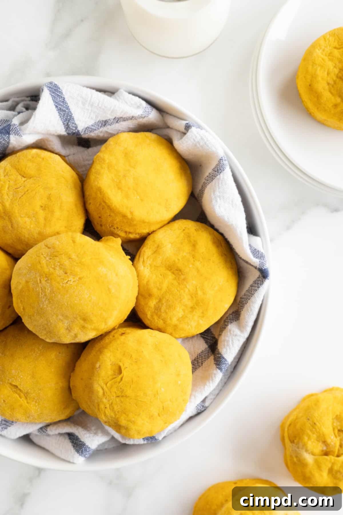 A large white serving bowl lined with a tea towel filled with freshly baked pumpkin biscuits, ready to be served.