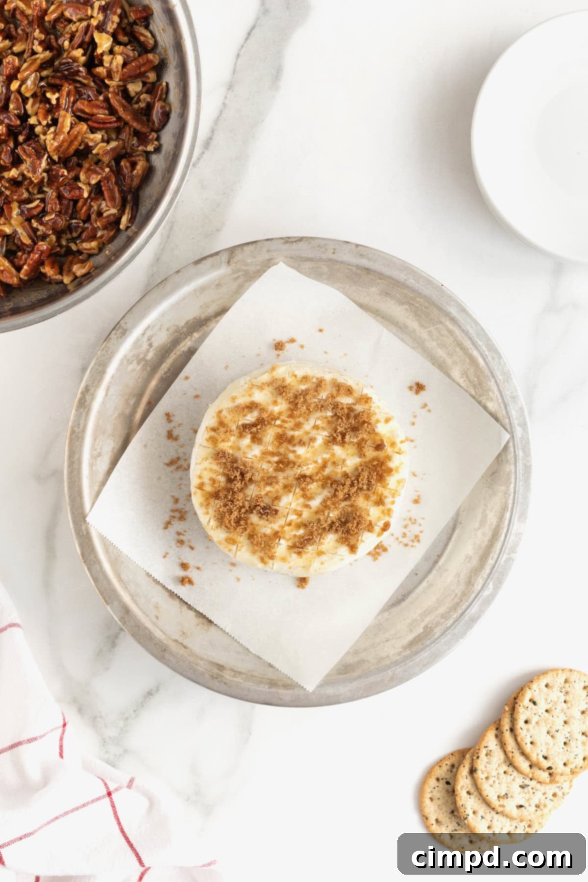 Caramel Pecan Baked Brie 7 A wheel of brie scored and sprinkled with brown sugar.