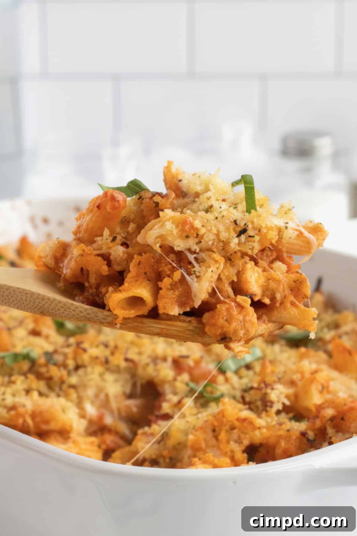 Chicken Parmesan Casserole being lifted from a white casserole dish on a wooden spoon.