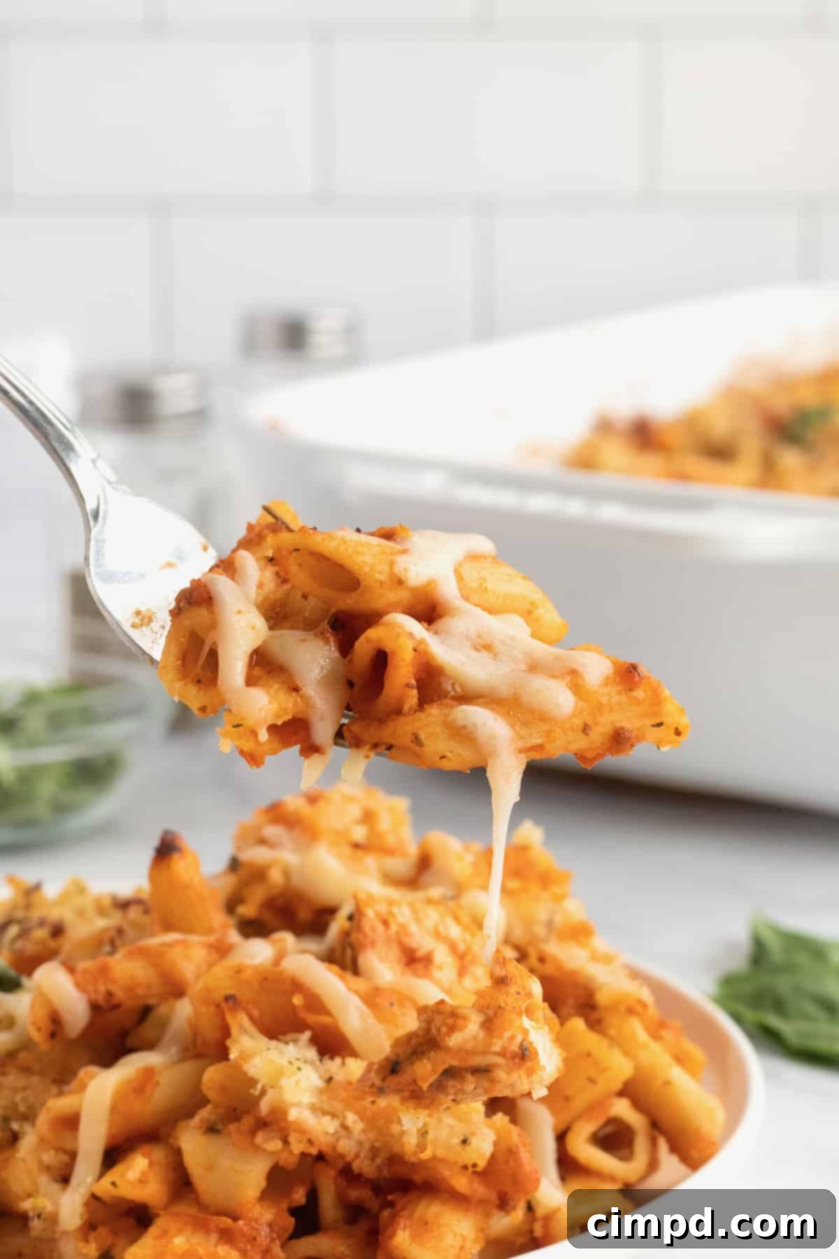 Chicken Parmesan Casserole on a fork in front of a plate of pasta.
