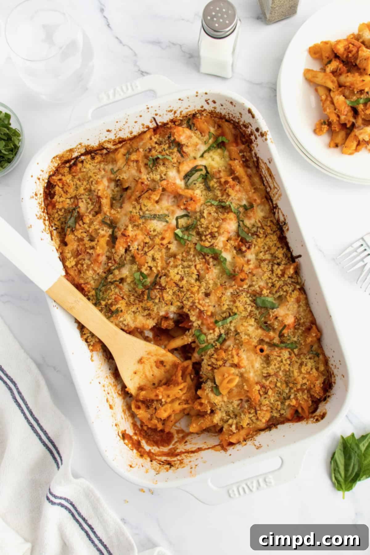 A white casserole dish of chicken parmesan casserole with a wooden spoon in it.