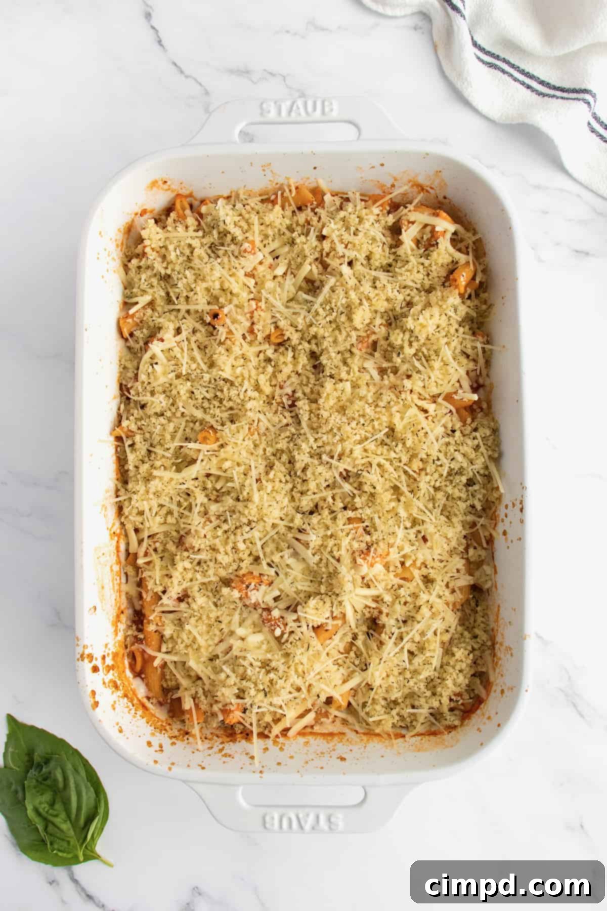 A white casserole dish of chicken parmesan casserole topped with parmesan and bread crumbs.