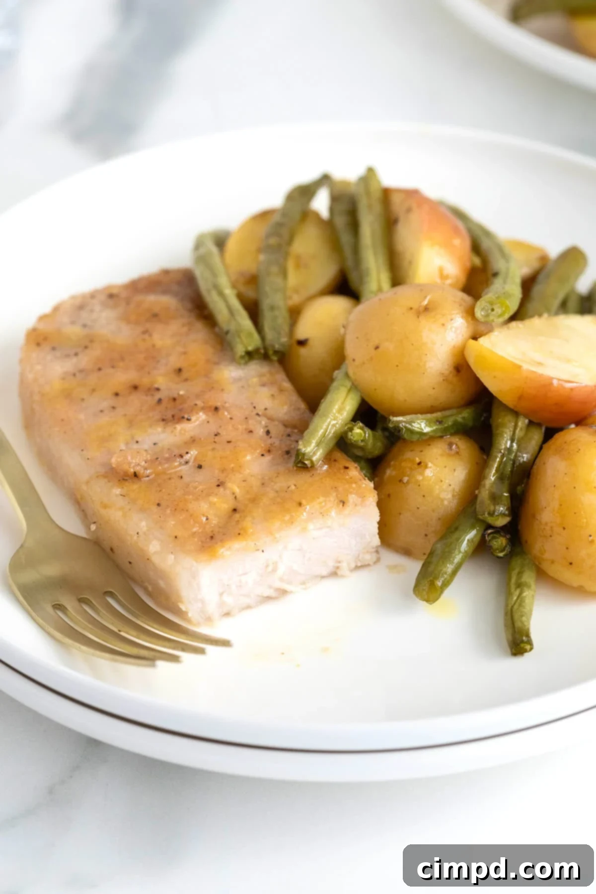A perfectly cooked pork chop on a pristine white dinner plate, artfully accompanied by golden roasted potatoes and crisp green beans, showcasing the deliciousness of the dish.
