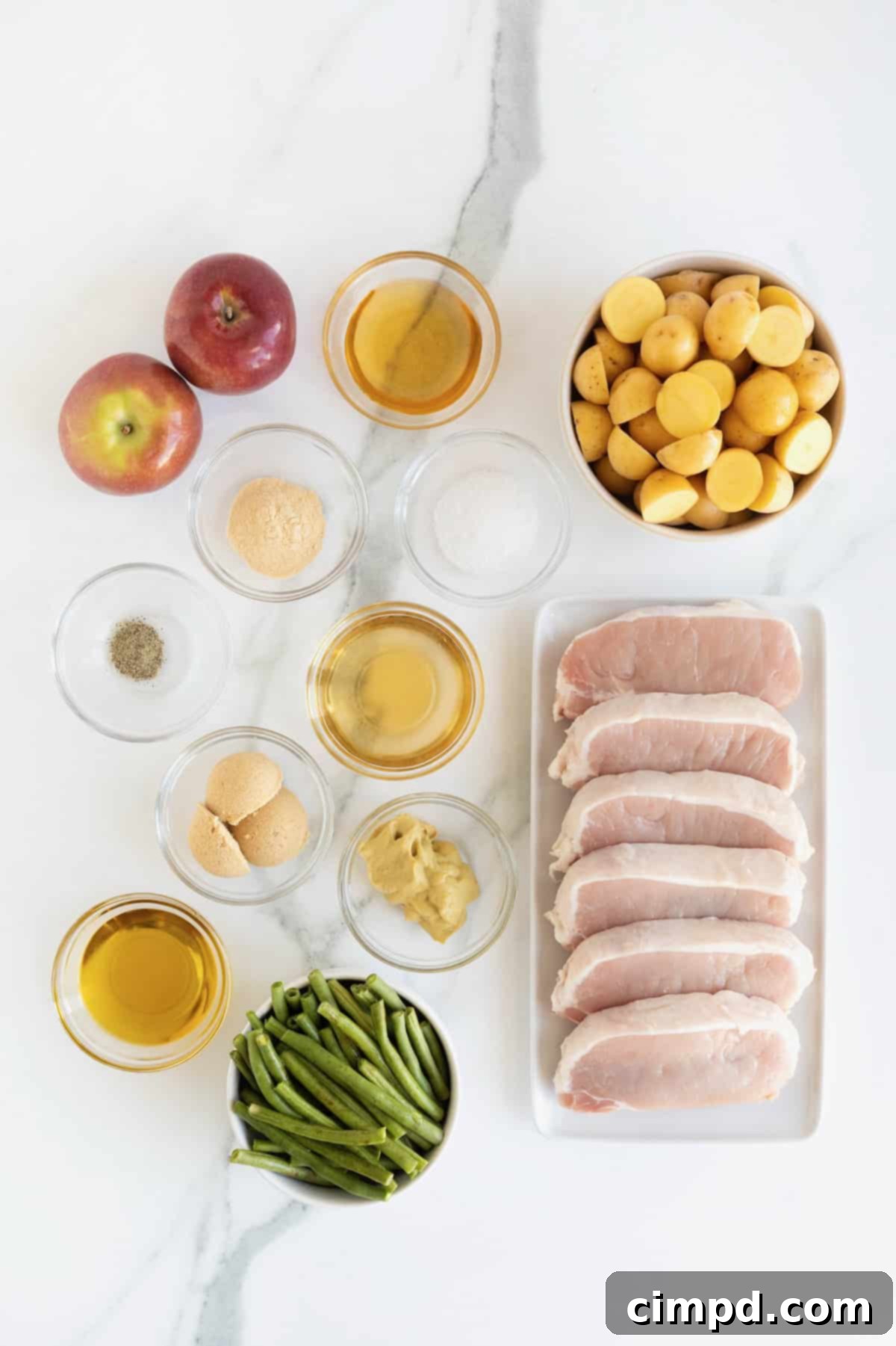 Various ingredients for sheet pan pork chops, neatly arranged in small glass dishes on a pristine white marble countertop, ready for preparation.