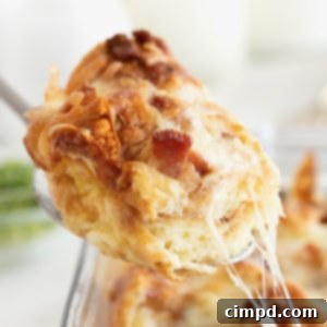 Golden Croissant Breakfast Bake 10 A spoonful of croissant breakfast casserole being lifted from a glass dish, showcasing the layers of croissant, egg, bacon, and cheese.