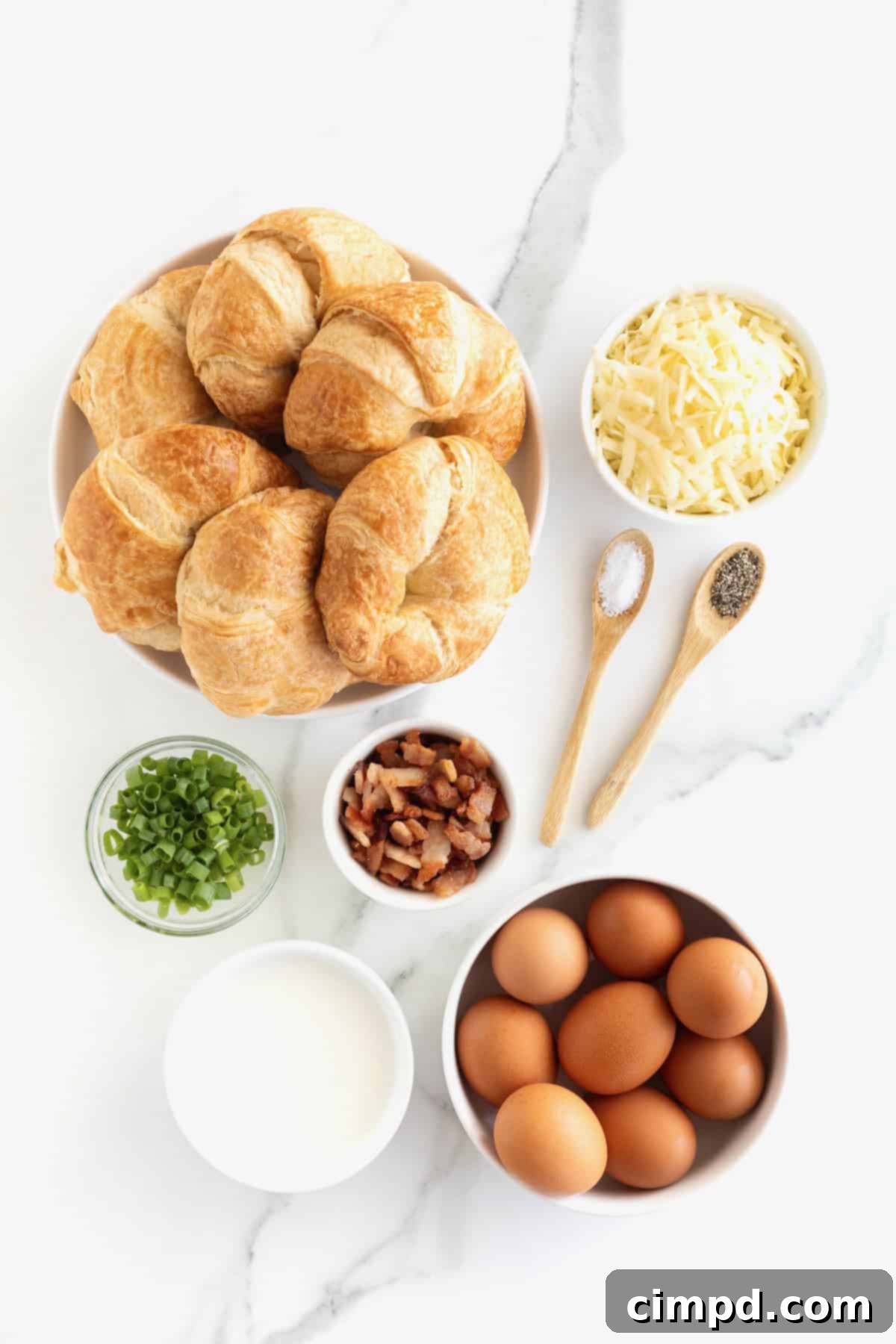 Golden Croissant Breakfast Bake 5 Ingredients for croissant breakfast casserole neatly arranged in glass dishes on a white marble counter, ready for preparation.