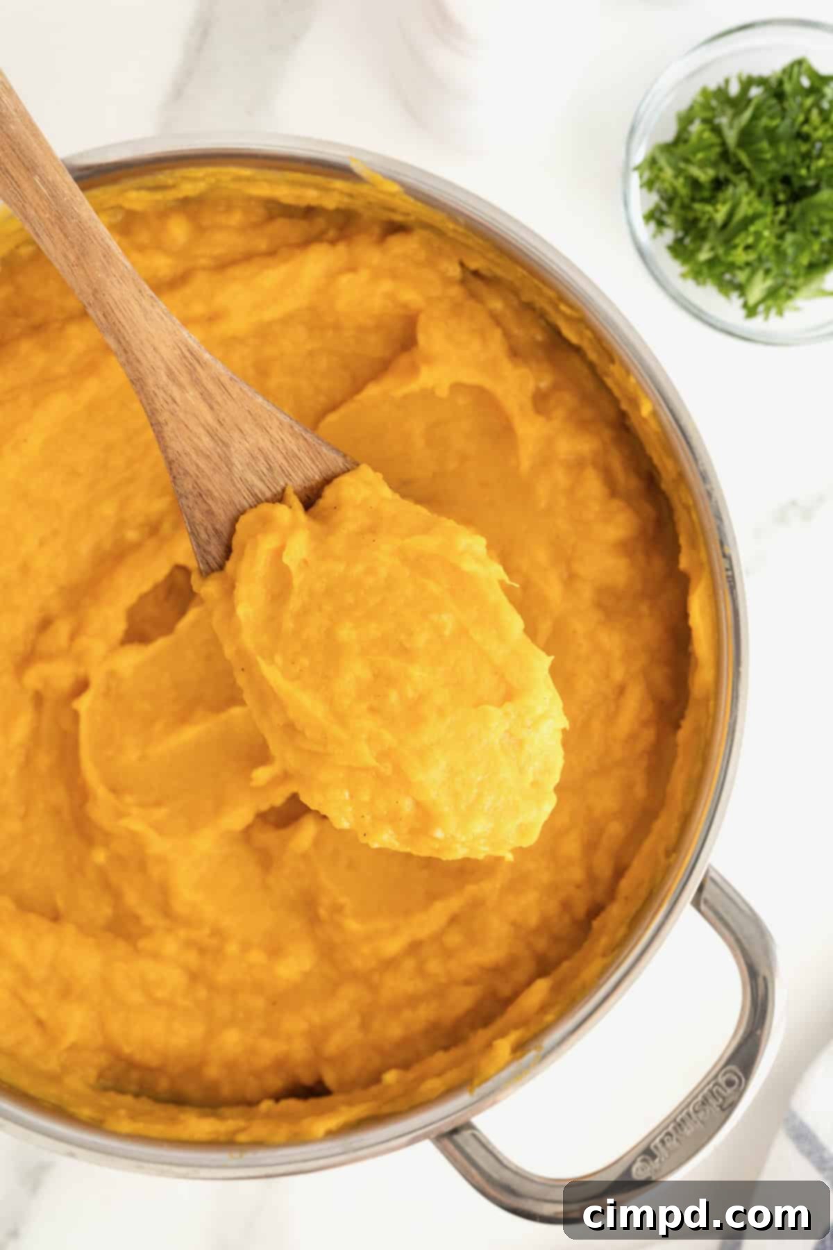 A stainless steel saucepan filled with perfectly mashed butternut squash, resting on a pristine white marble counter, showcasing its smooth, creamy texture.