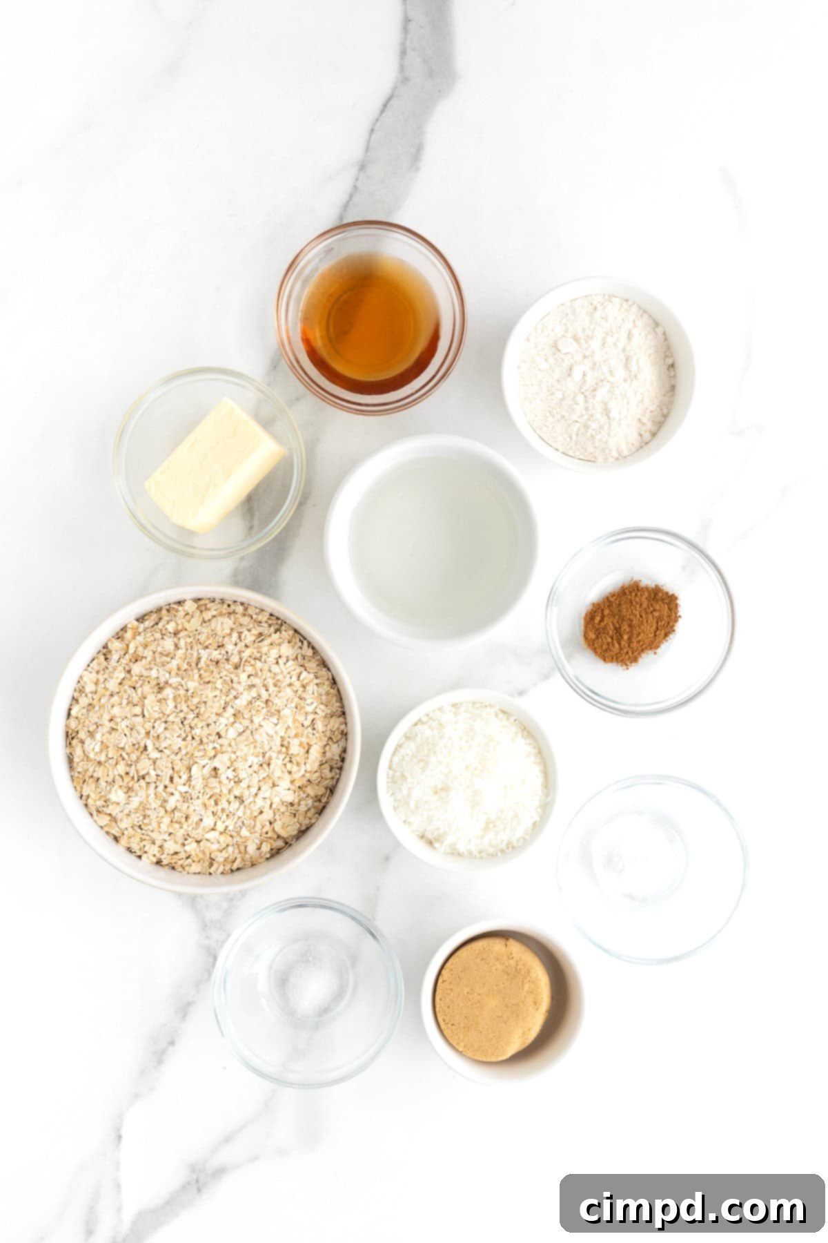 Ingredients to make oatmeal crunchies displayed in small glass dishes on a white marble counter, neat and ready for use.