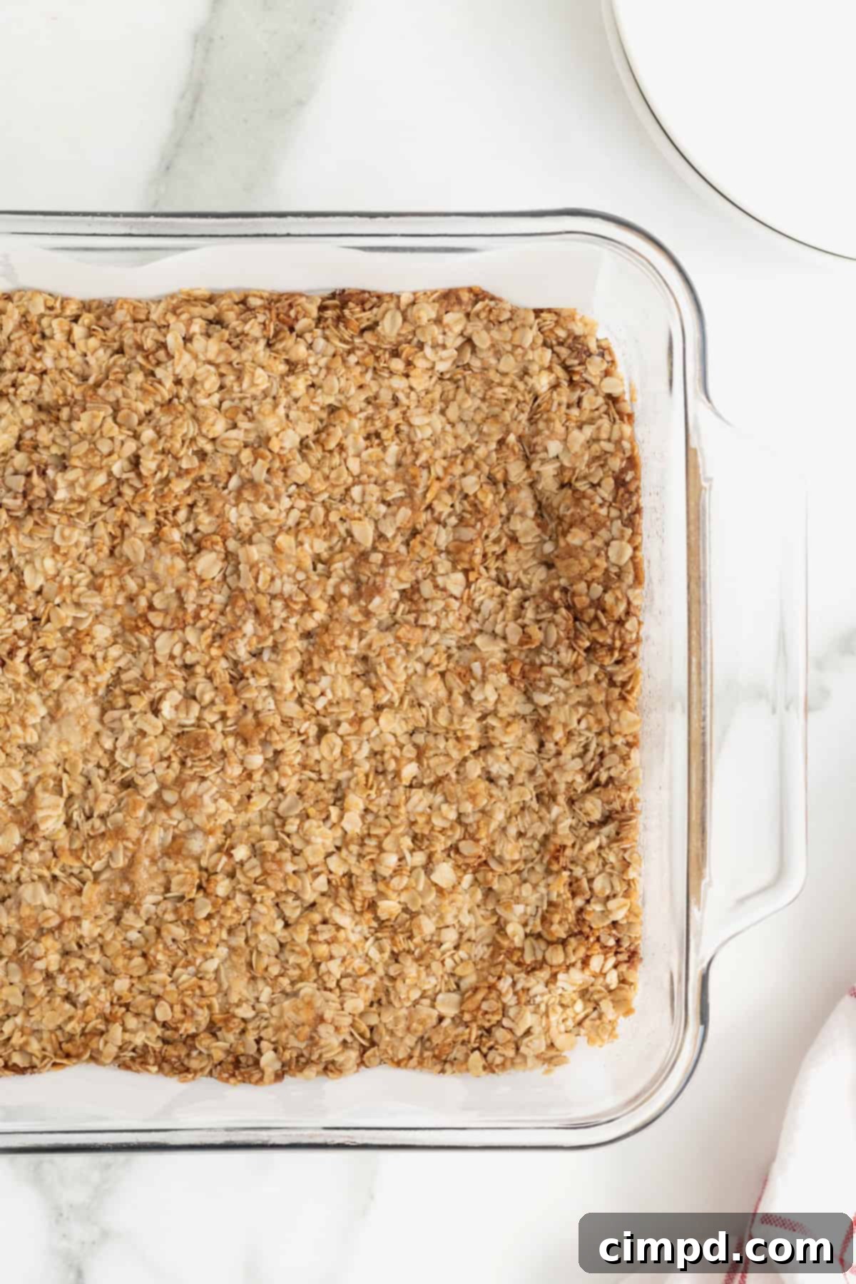 A glass baking dish filled with freshly baked oatmeal crunchies on a white marble counter, ready for storage.