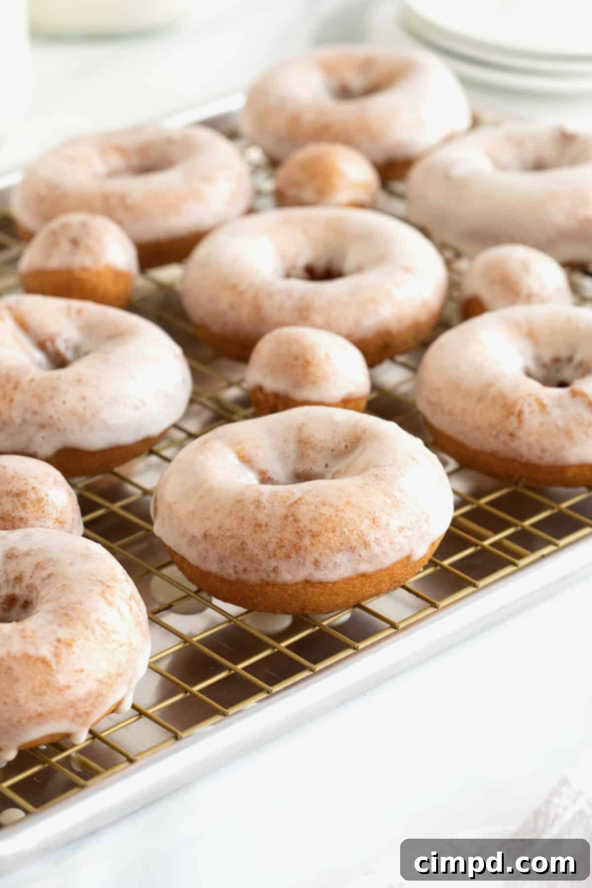 Homemade glazed donuts on a cooling rack over an aluminum sheet pan.