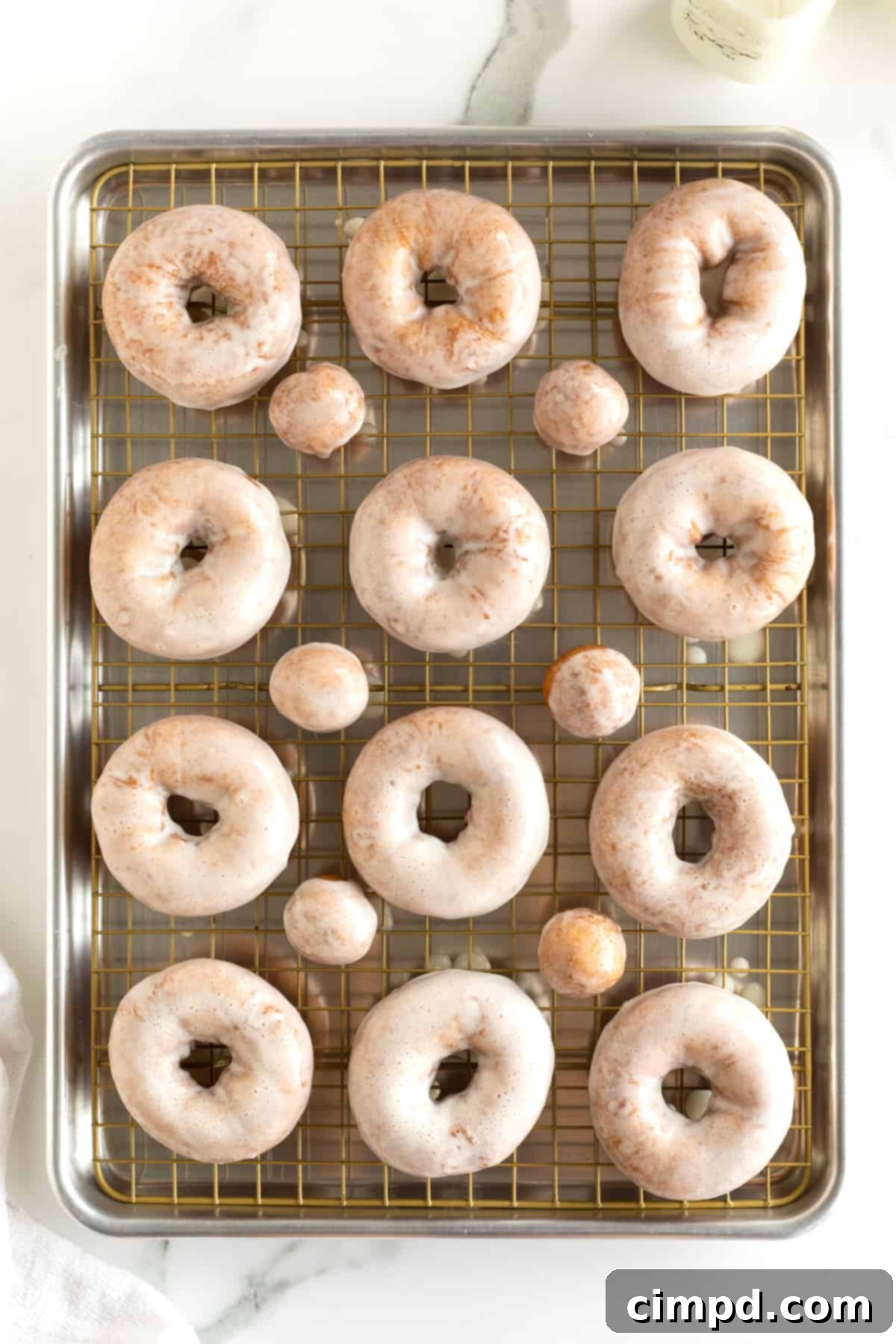 12 glazed donuts and six glazed donut holes on an aluminum baking sheet.