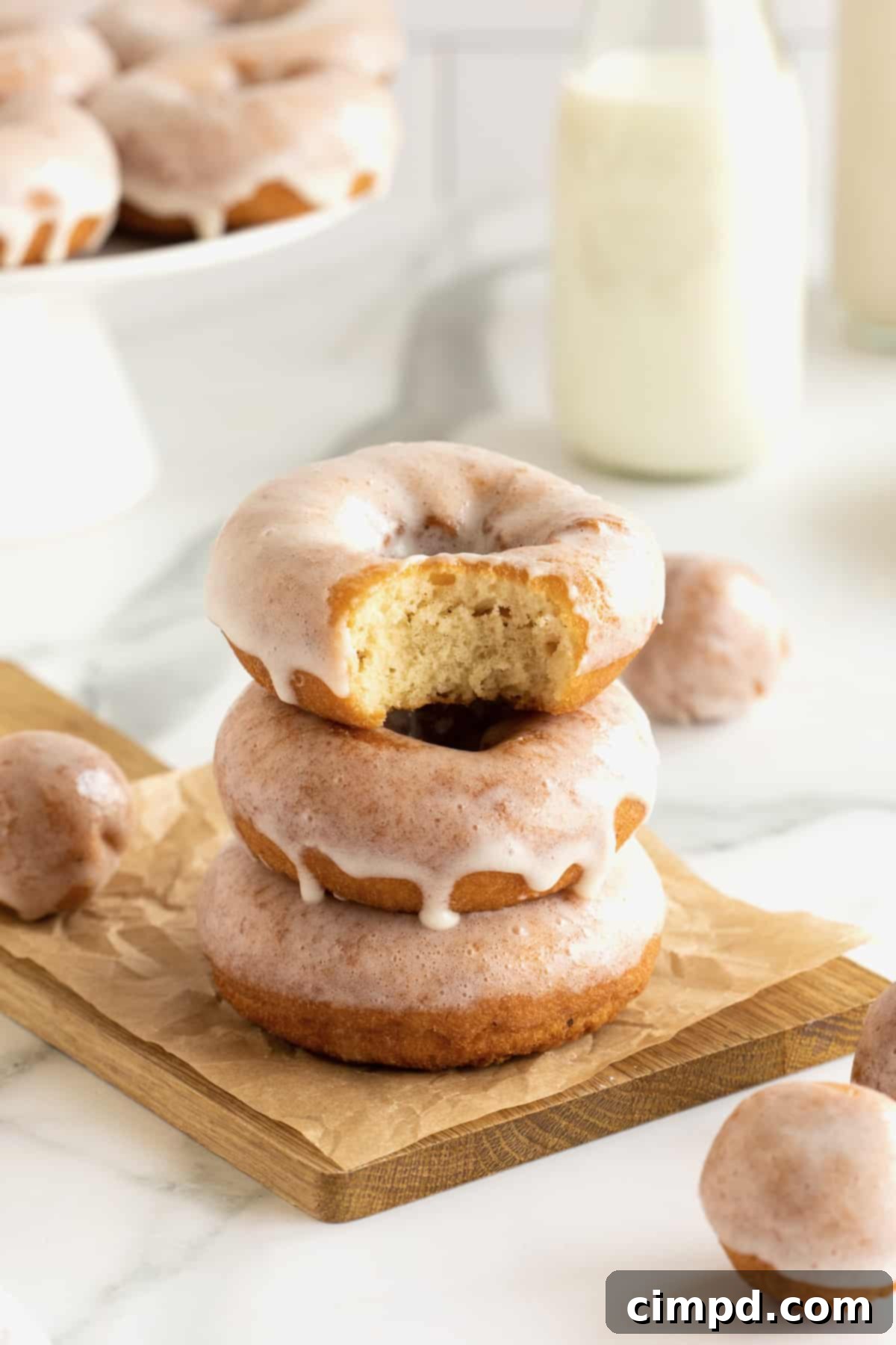 Three glazed homemade donuts stacked on a wooden cutting board.