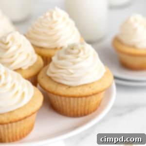The Perfect Classic Vanilla Cupcake 12 Four vanilla cupcakes with white icing on a white cake stand.