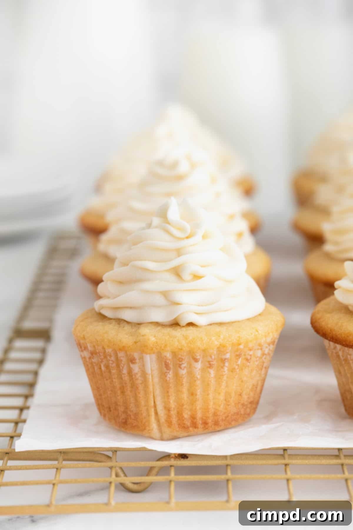 The Perfect Classic Vanilla Cupcake 4 Eight perfectly frosted vanilla cupcakes neatly arranged on a parchment-lined cooling rack, showcasing their pristine white icing.