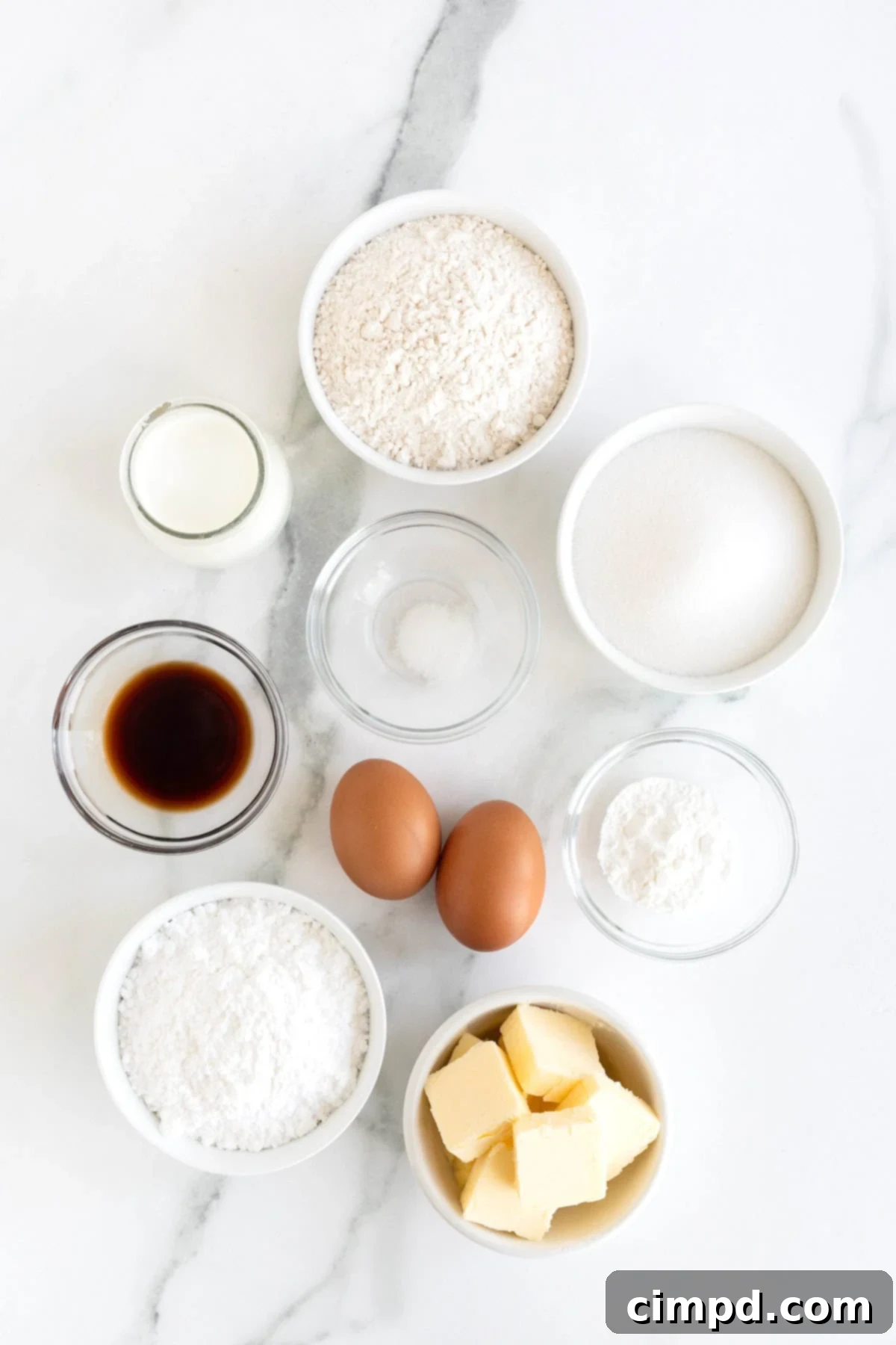 The Perfect Classic Vanilla Cupcake 5 All ingredients laid out in small white and glass dishes on a white marble counter, showcasing their freshness and organization.