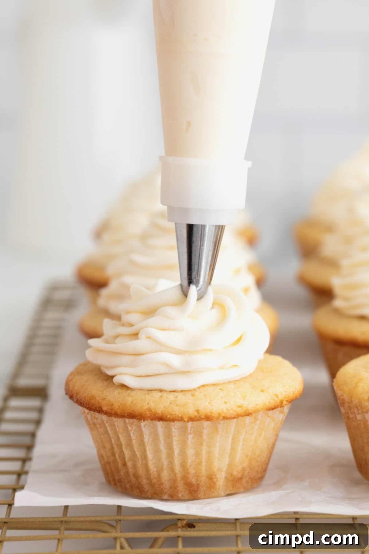 The Perfect Classic Vanilla Cupcake 9 Rich vanilla frosting being expertly piped onto a classic vanilla cupcake nestled in a pristine white paper wrapper, ready for enjoyment.