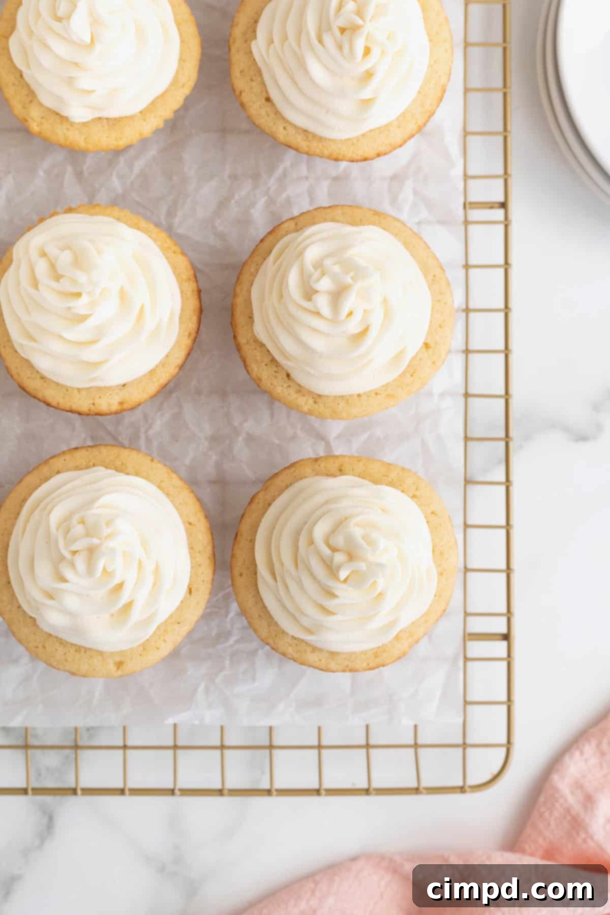 The Perfect Classic Vanilla Cupcake 10 Six beautifully frosted vanilla cupcakes sitting on a parchment-lined cooling rack, showcasing their pristine appearance ready for storage.