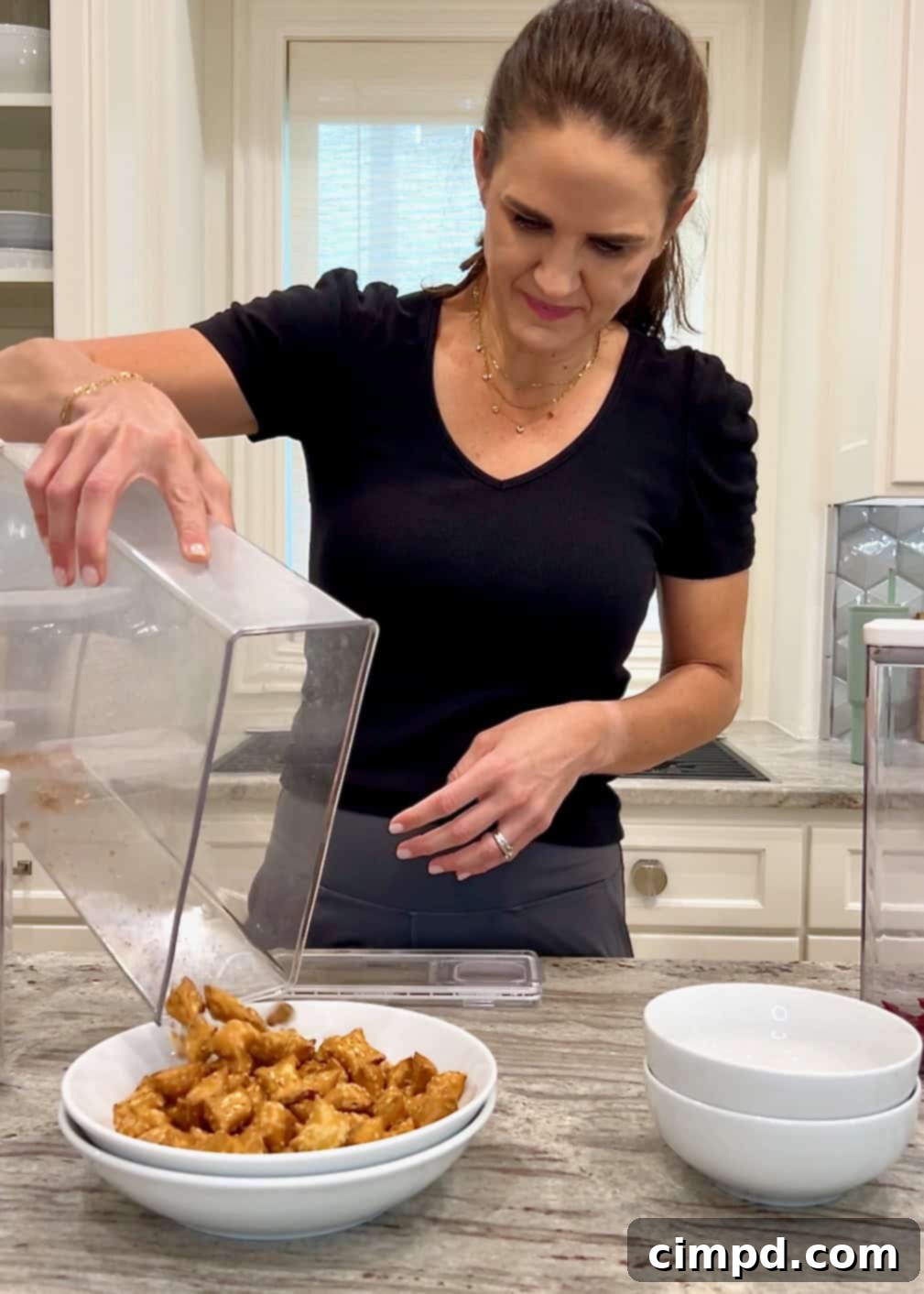 Close-up shot of Maegan Brown pouring cereal from a clear, labeled canister into a large bowl, illustrating the decluttering process.
