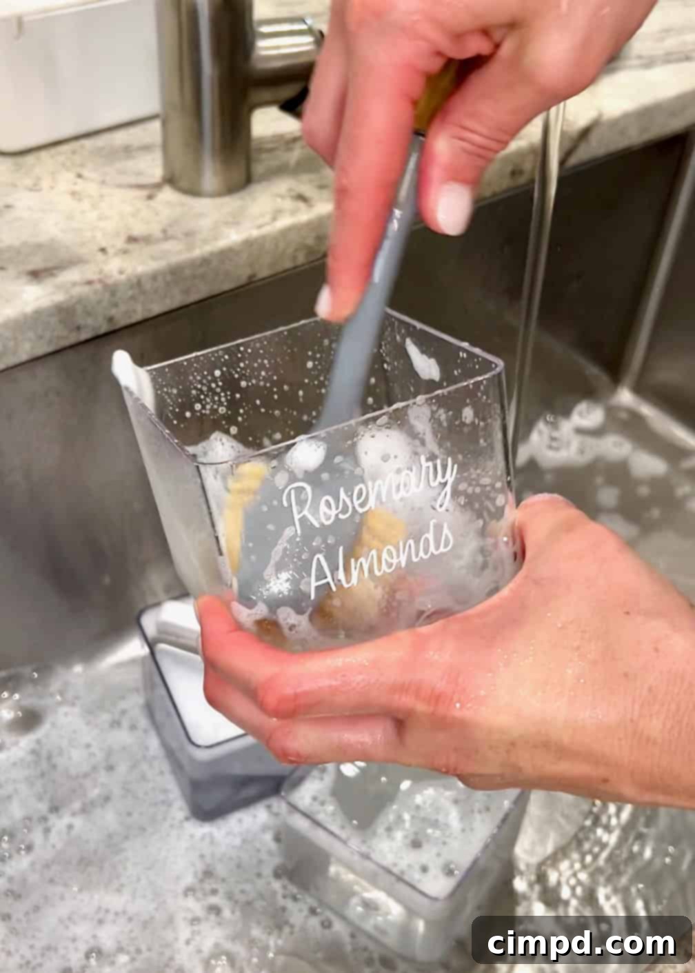 A hand using a scrub brush to meticulously clean a clear storage container in a sink, highlighting the importance of hygiene.