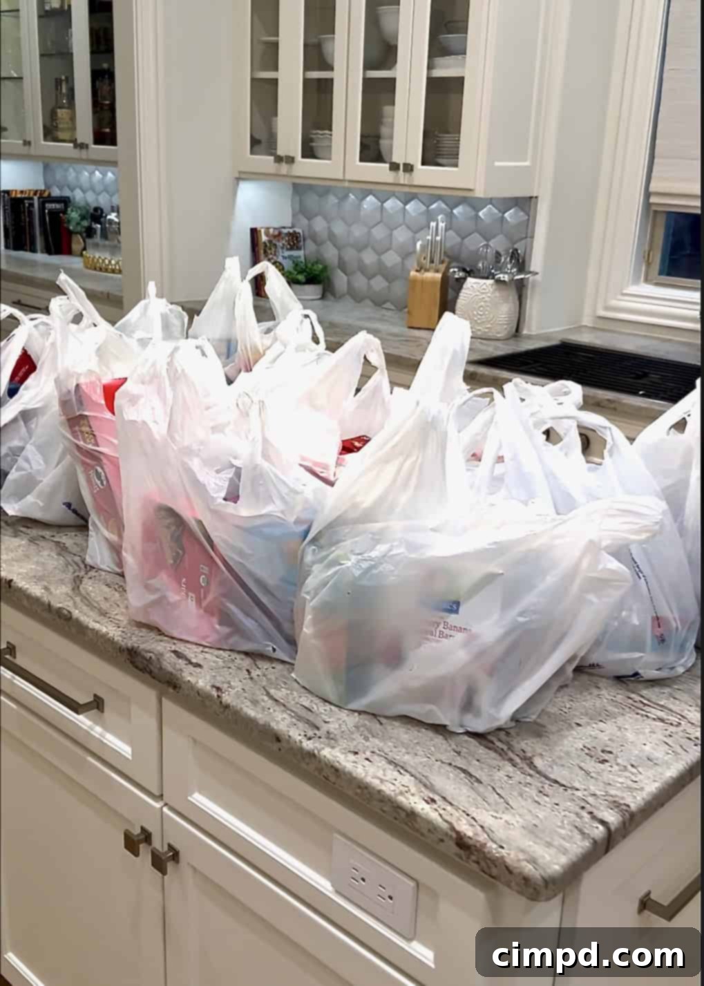 Reusable plastic grocery bags filled with fresh produce and pantry items resting on a sleek gray and brown marble kitchen counter after a shopping trip.