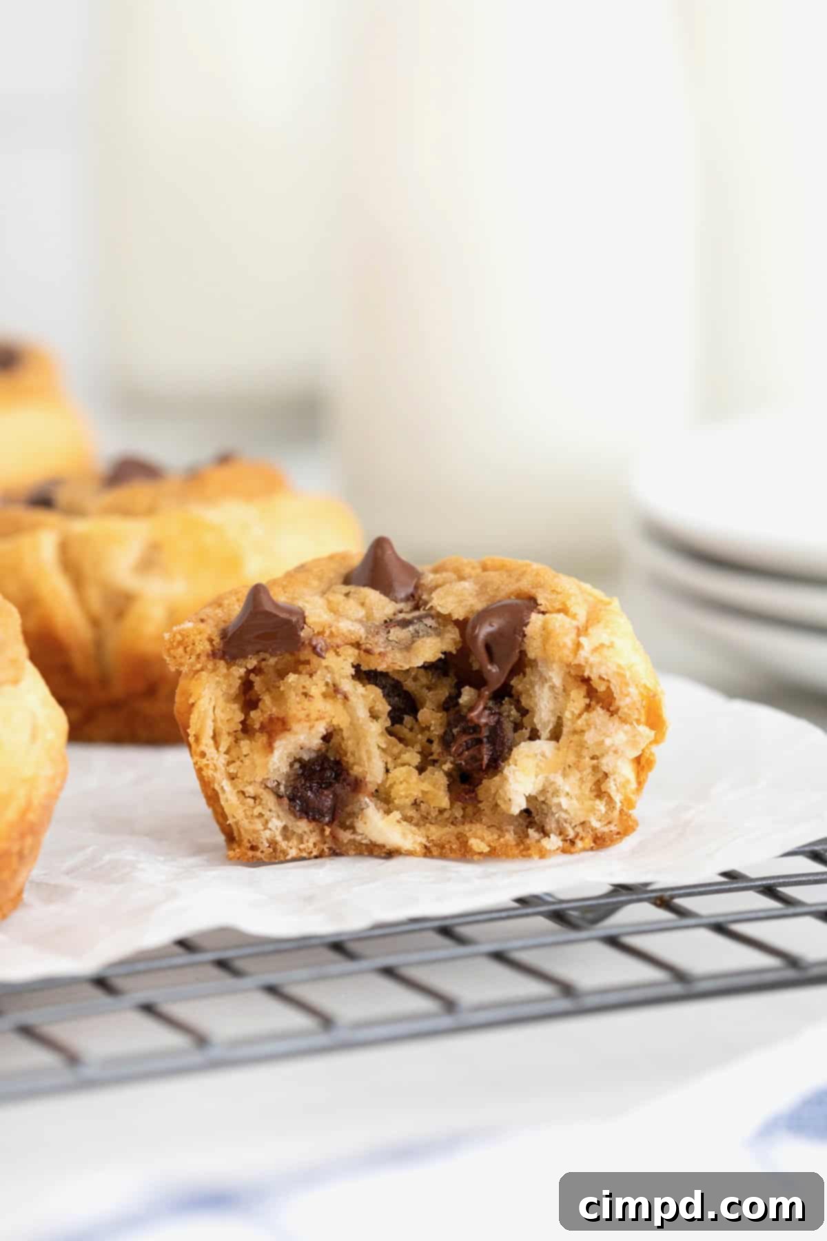 A chocolate chip cookie dough cruffin on a parchment lined cooling rack. The cruffin is cut in half revealing the inside layers.