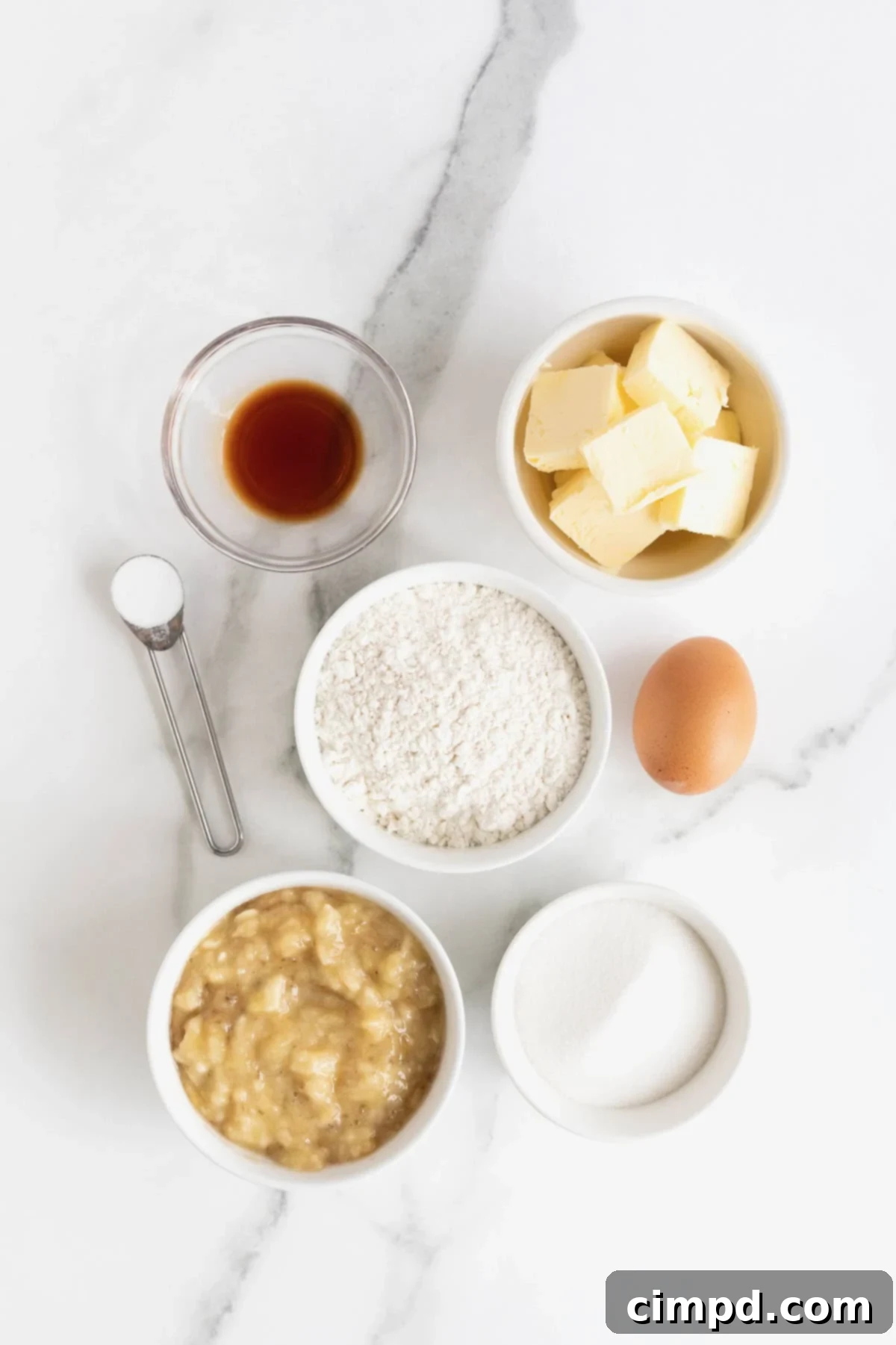 A collection of ingredients for banana muffins, neatly arranged in small white dishes on a pristine white marble counter, ready for baking.