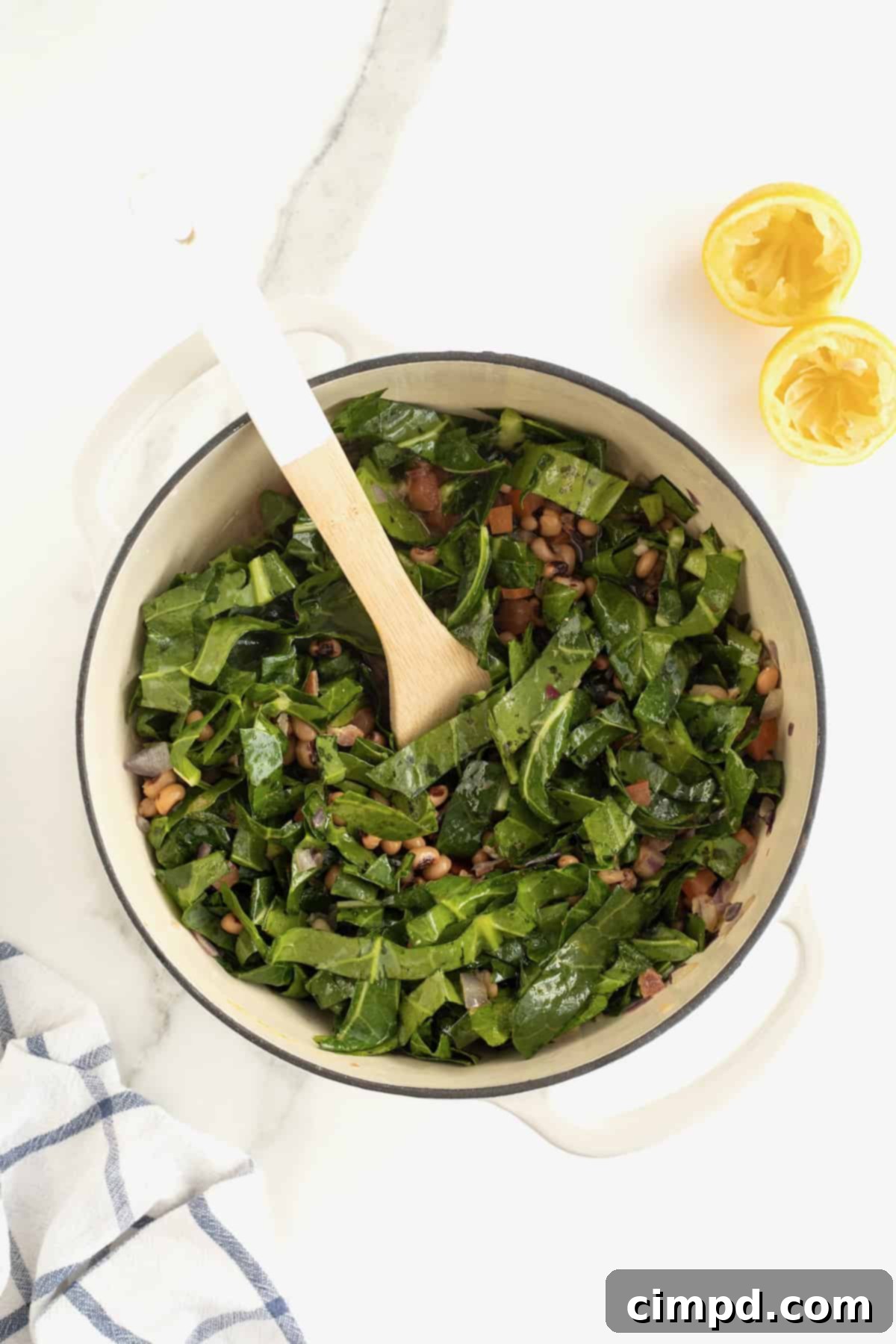 Warm chicken broth being carefully stirred into a large, simmering pot containing a vibrant mixture of collard greens, black eyed peas, and other aromatic ingredients, showcasing a critical stage of the cooking process.