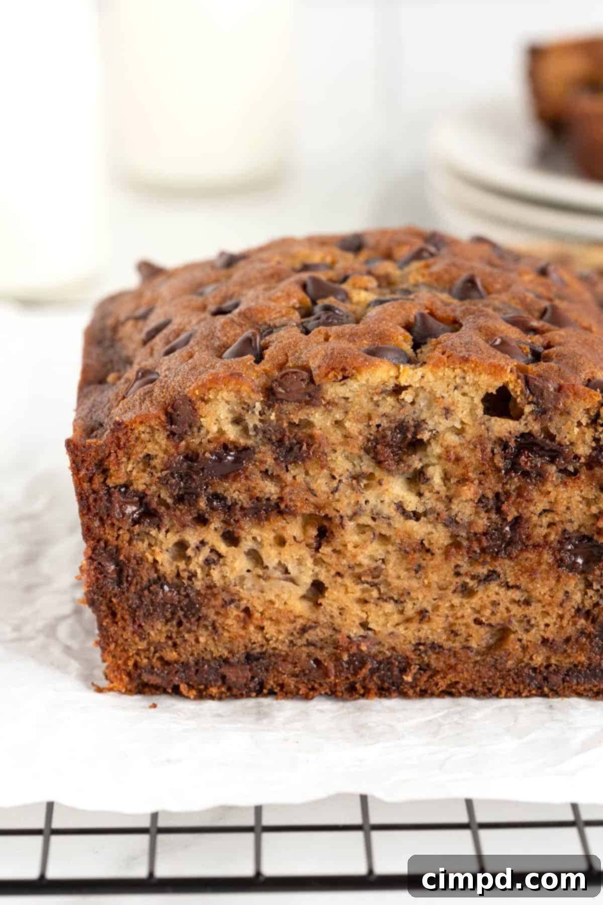 A whole loaf of chocolate chip banana bread, richly golden and studded with chocolate, cooling on a parchment-lined wire rack.