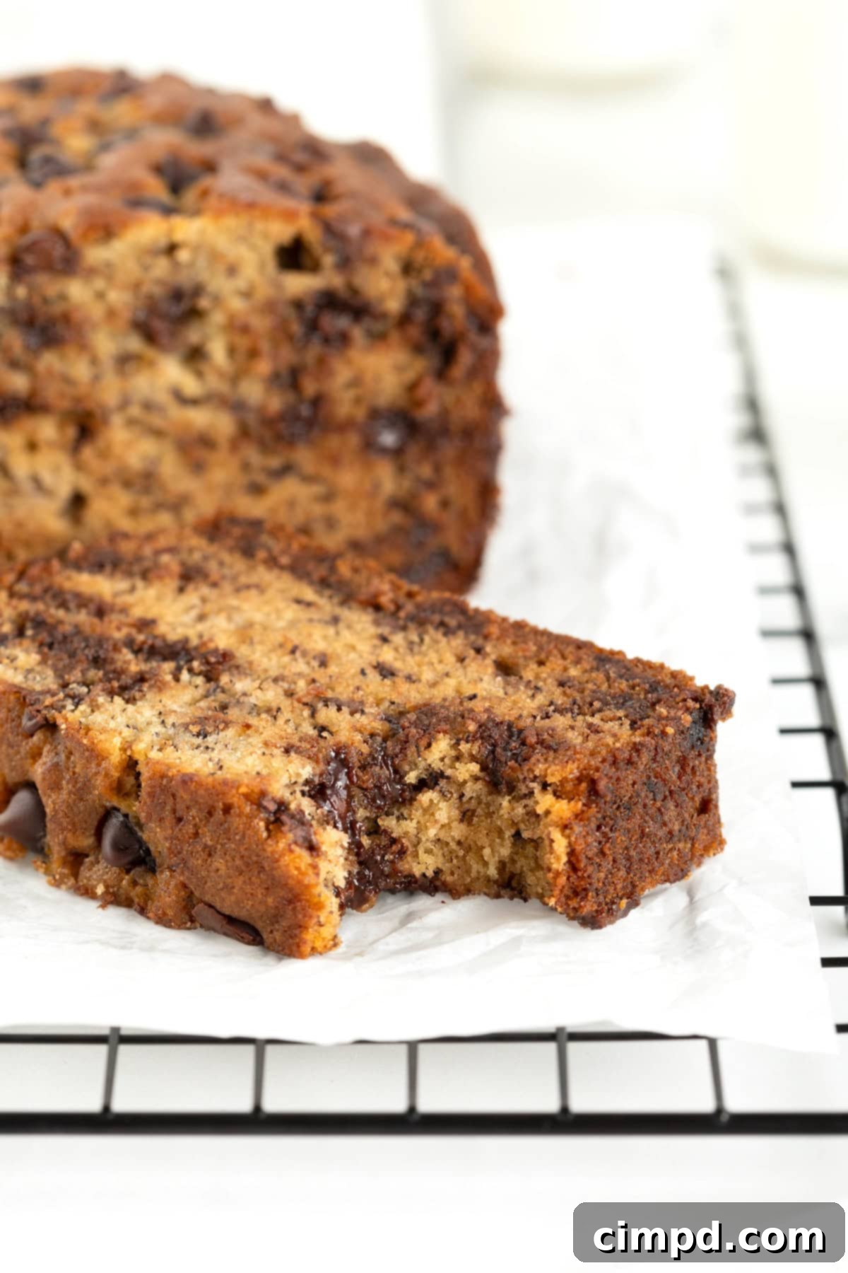 A single, perfectly baked slice of chocolate chip banana bread on a parchment-lined cooling rack, with a small bite taken out, showcasing its moist crumb and melted chocolate.