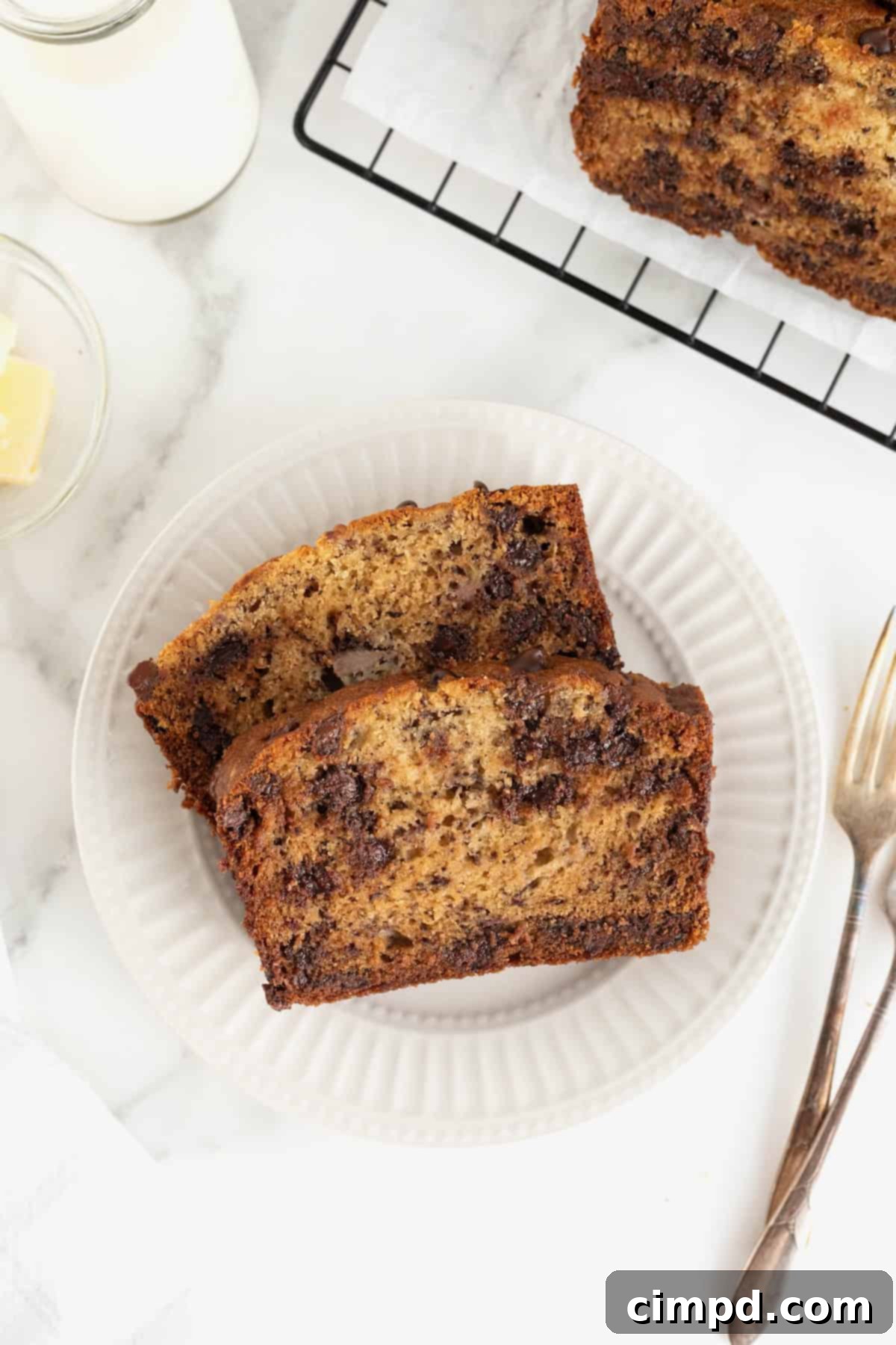Two generous slices of chocolate chip banana bread arranged on a delicate fluted white plate, ready to be enjoyed.