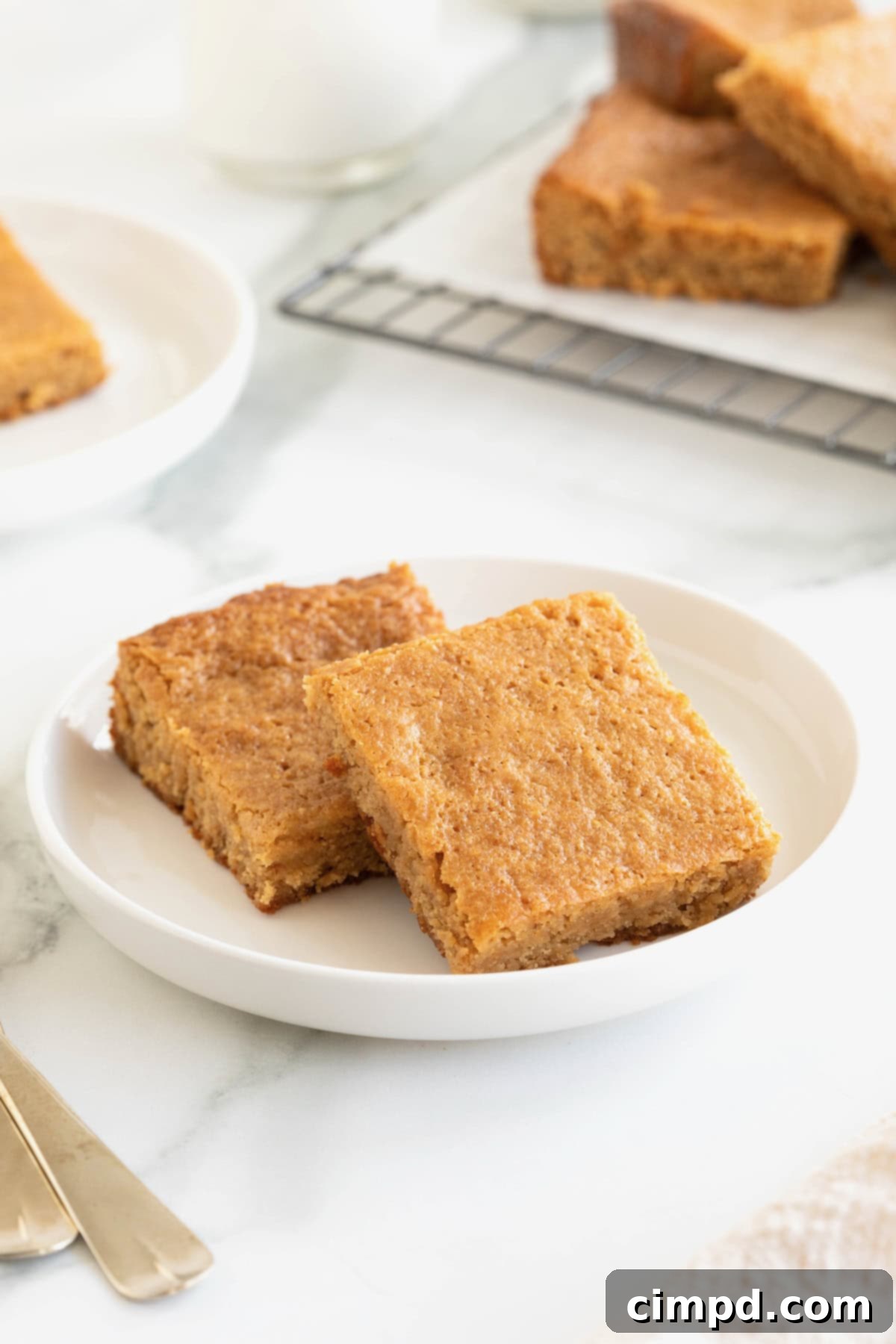 Two peanut butter brownies on a small white rimmed plate on a white marble counter, showcasing their golden-brown tops and moist texture.