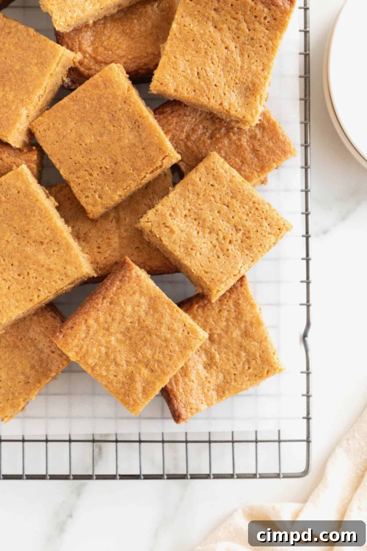 A delightful pile of peanut butter blondies, stacked on a parchment-lined cooling rack, enticing viewers with their golden hue.