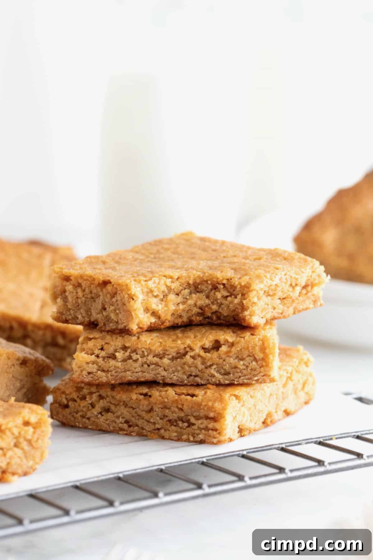 Three golden peanut butter blondies stacked neatly on a parchment-lined cooling rack, highlighting their soft texture and inviting color.