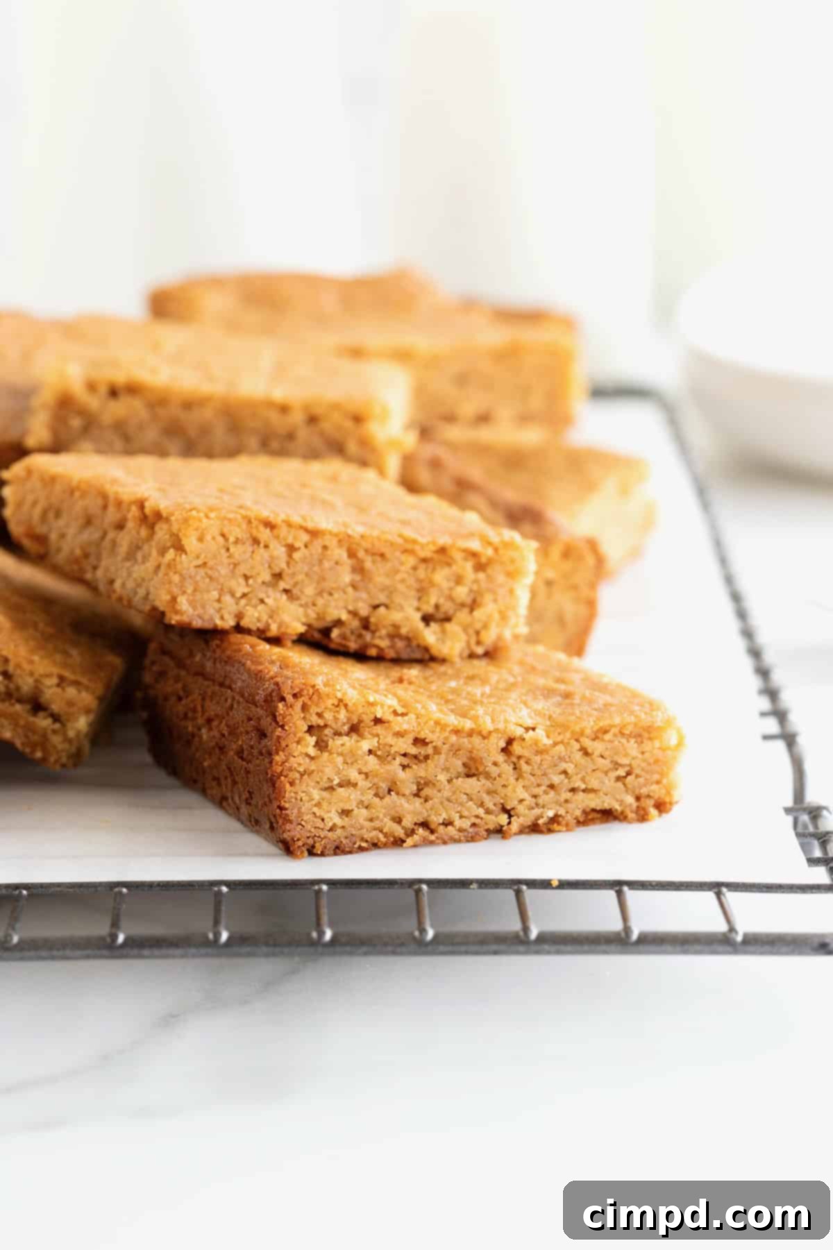 Three perfectly stacked peanut butter blondies resting on a parchment-lined cooling rack, demonstrating their enticing texture.