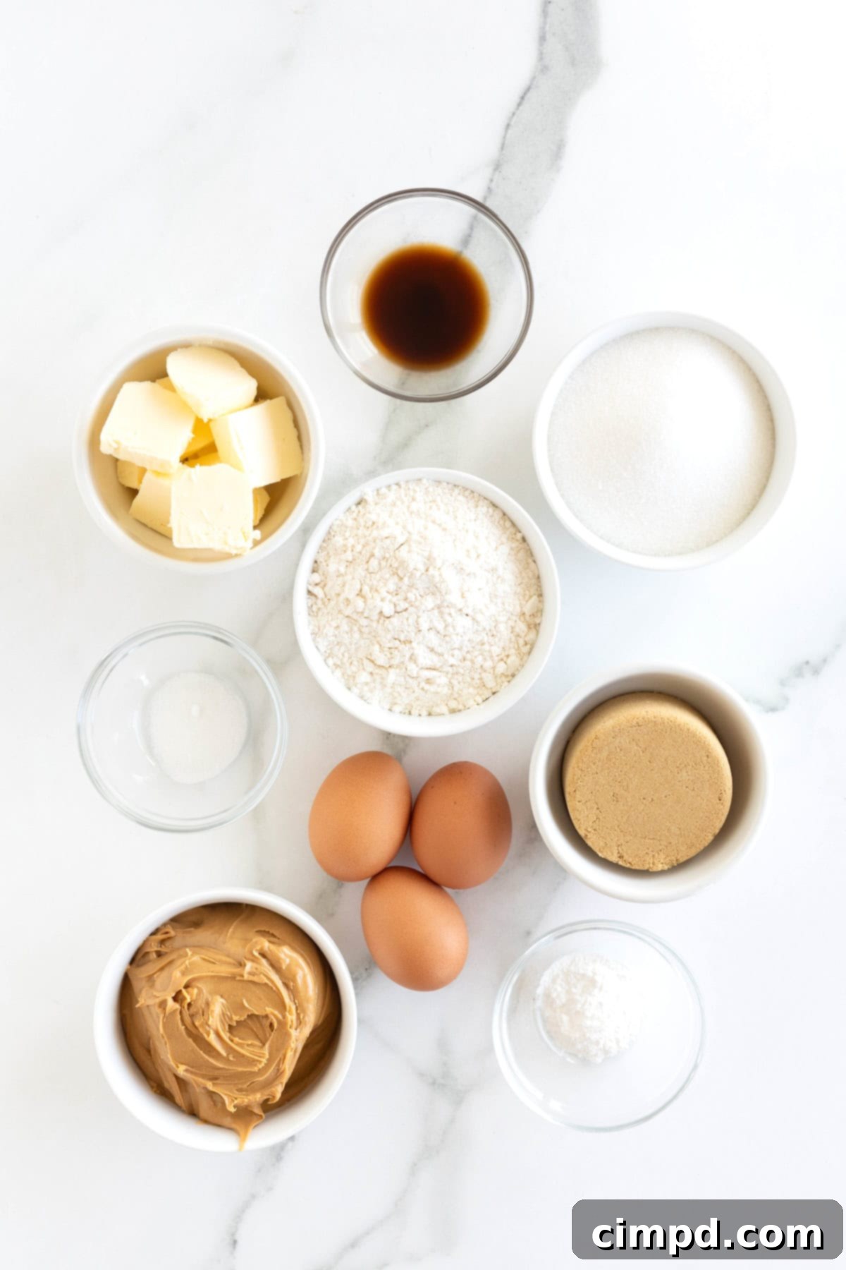 Various ingredients for peanut butter blondies neatly arranged in small glass dishes on a pristine white marble counter, ready for baking.