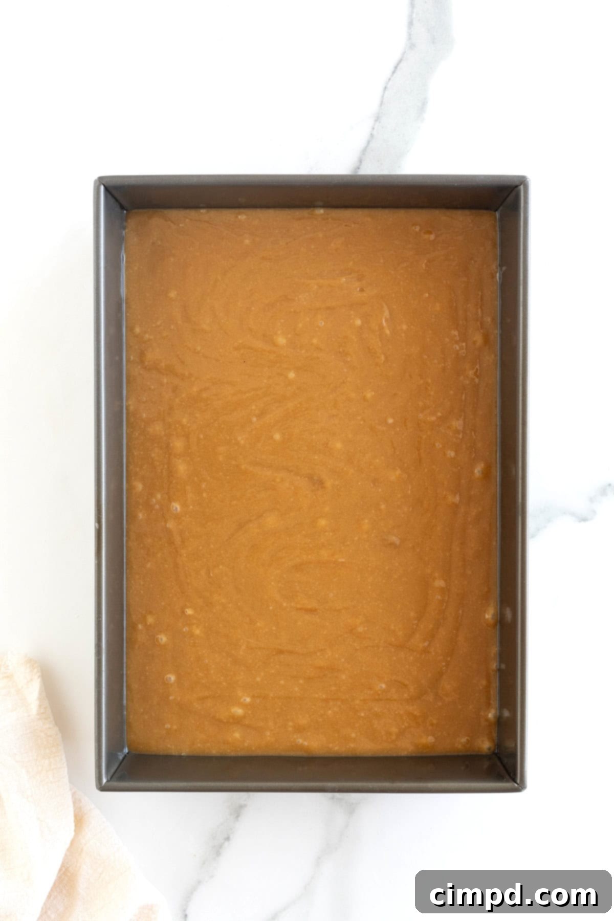 A dark aluminum baking pan filled with smooth peanut butter blondie batter, resting on a white marble counter, ready for the oven.