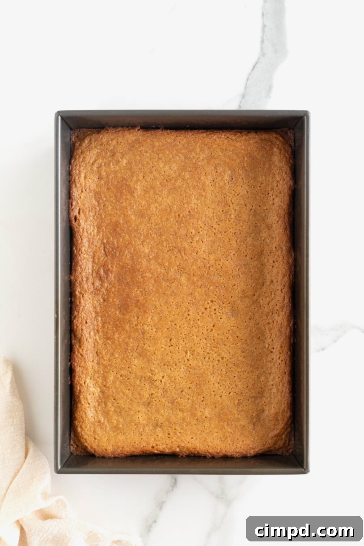 A freshly baked dark aluminum pan of peanut butter blondies with a golden crust, cooling on a white marble counter.