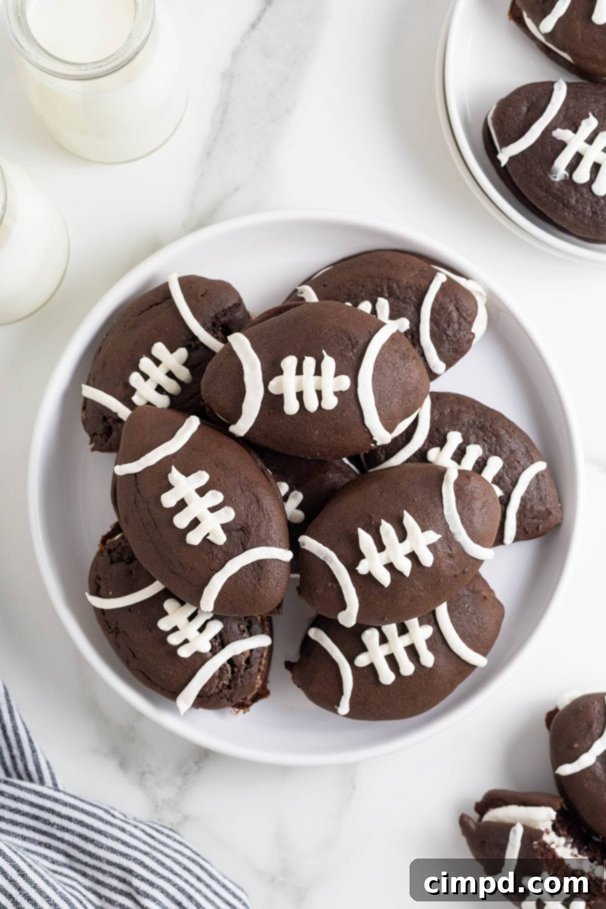 A large white platter of chocolate whoopie pies decorated like footballs.