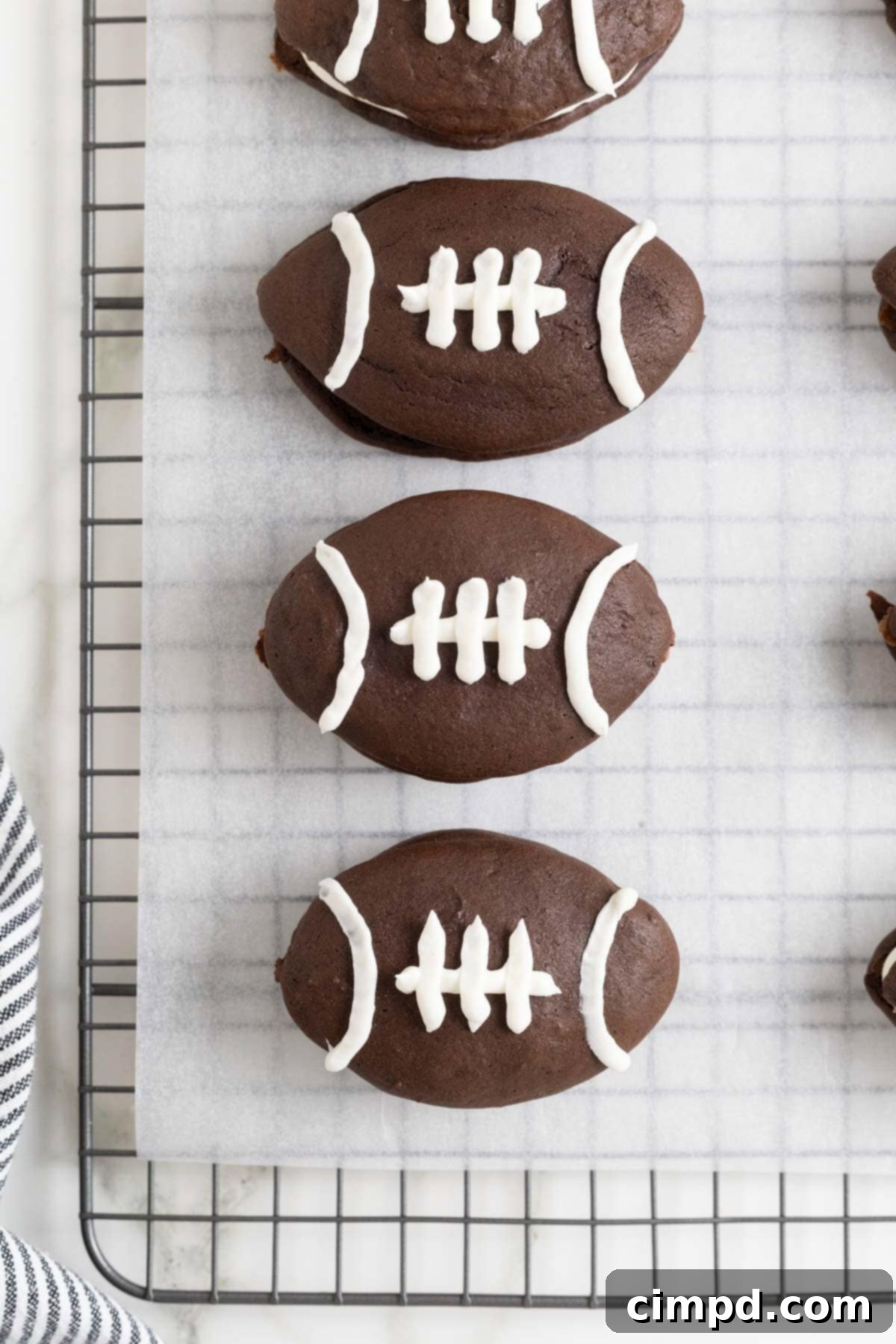 Four football shaped chocolate whoopie pies on a parchment lined cooling rack.