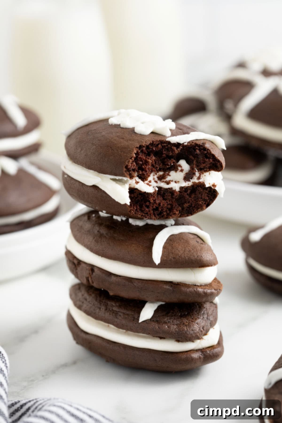 A stack of three football shaped whoopie pies on a white marble counter. The top one has a bite out of it.