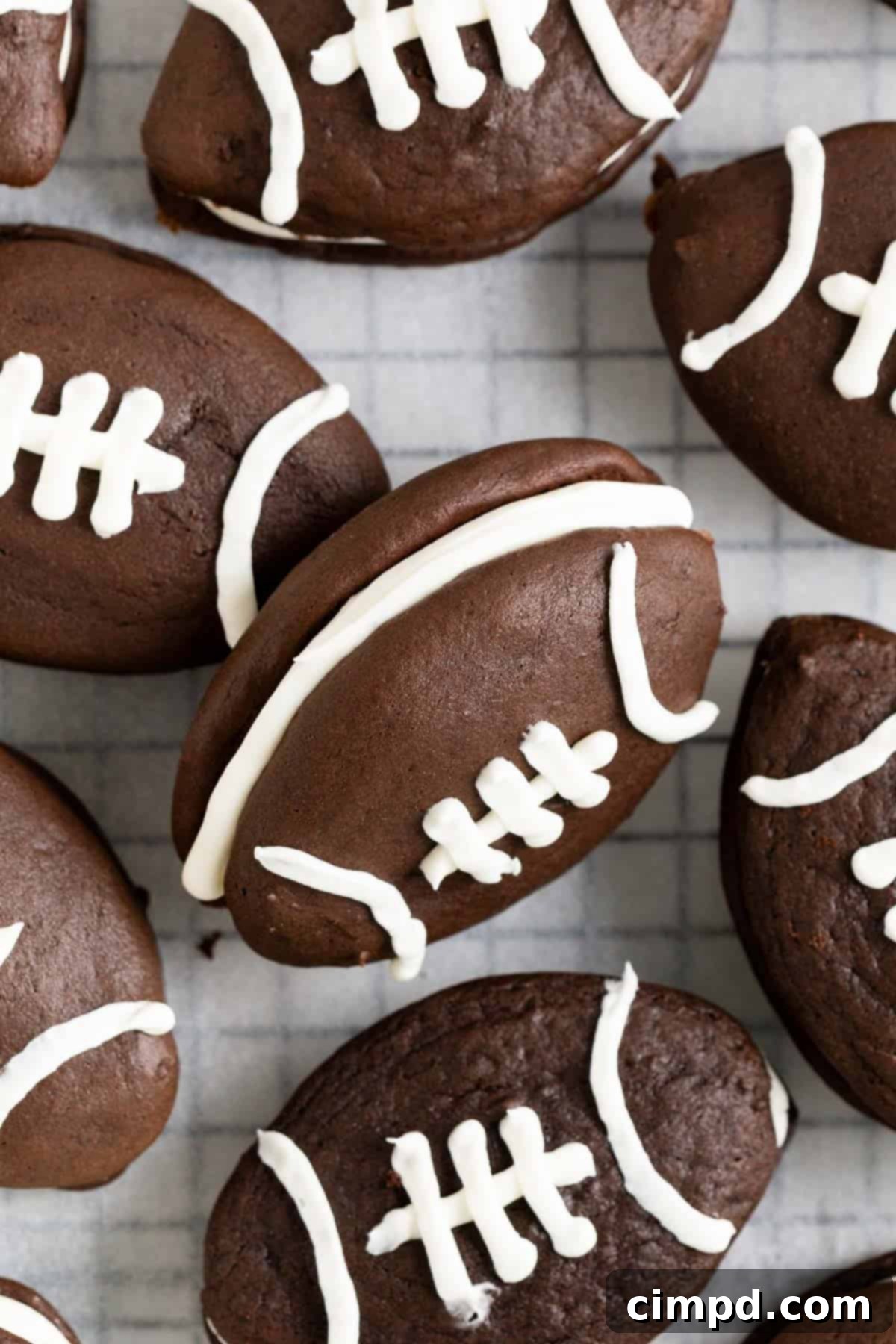 A pile of football shaped chocolate whoopie pies on a parchment lined wire cooling rack.
