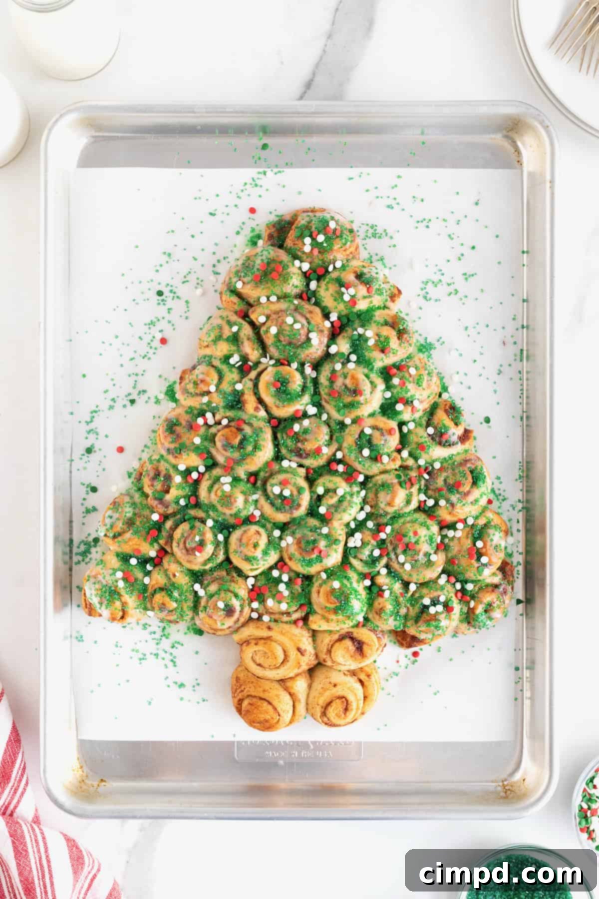A pull-apart cinnamon roll shaped like a Christmas tree, garnished with festive green and red sprinkles.