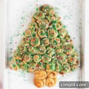 A pull-apart cinnamon roll shaped like a Christmas tree, garnished with festive green and red sprinkles.