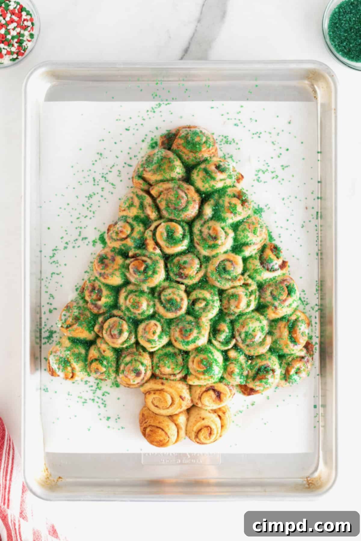A cinnamon roll Christmas tree sprinkled with vibrant green sugar crystals on a parchment lined baking sheet, ready for more decoration.