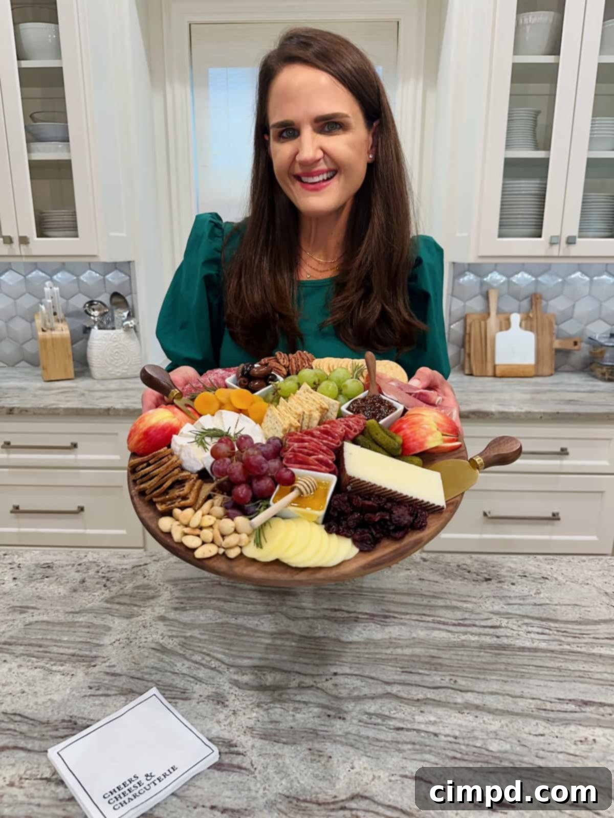 Maegan Brown gracefully presents a beautifully arranged round charcuterie board, filled with an assortment of gourmet delights, perfect for any gathering.